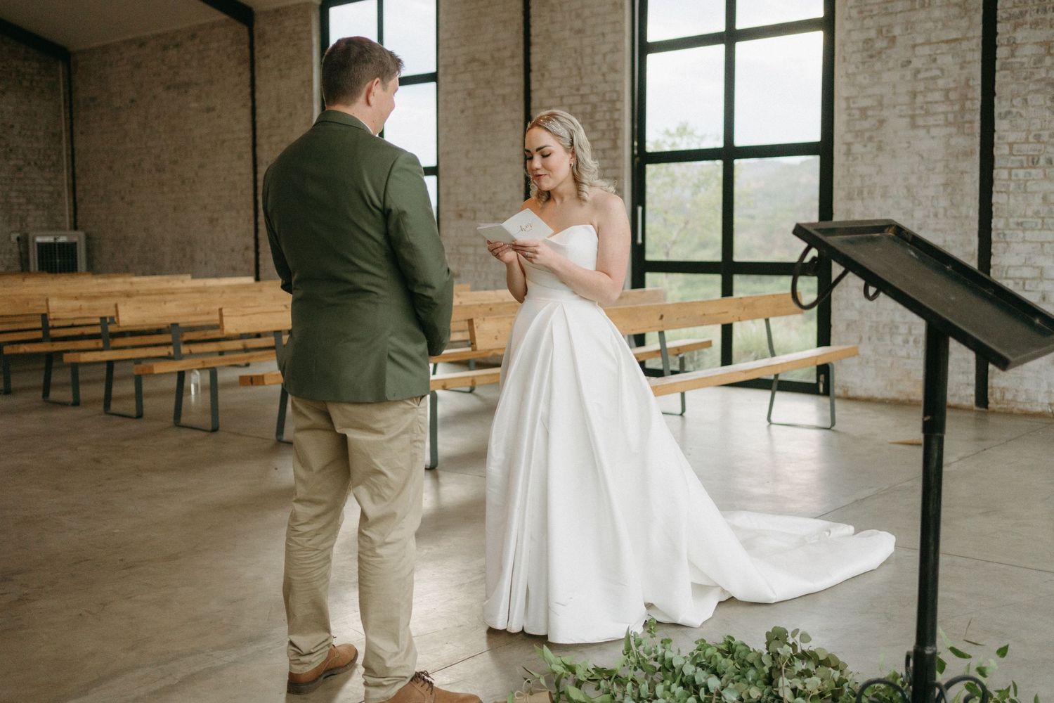 A wedding scene in an industrial-style venue with white gown and casual attire in front of wooden benches.
