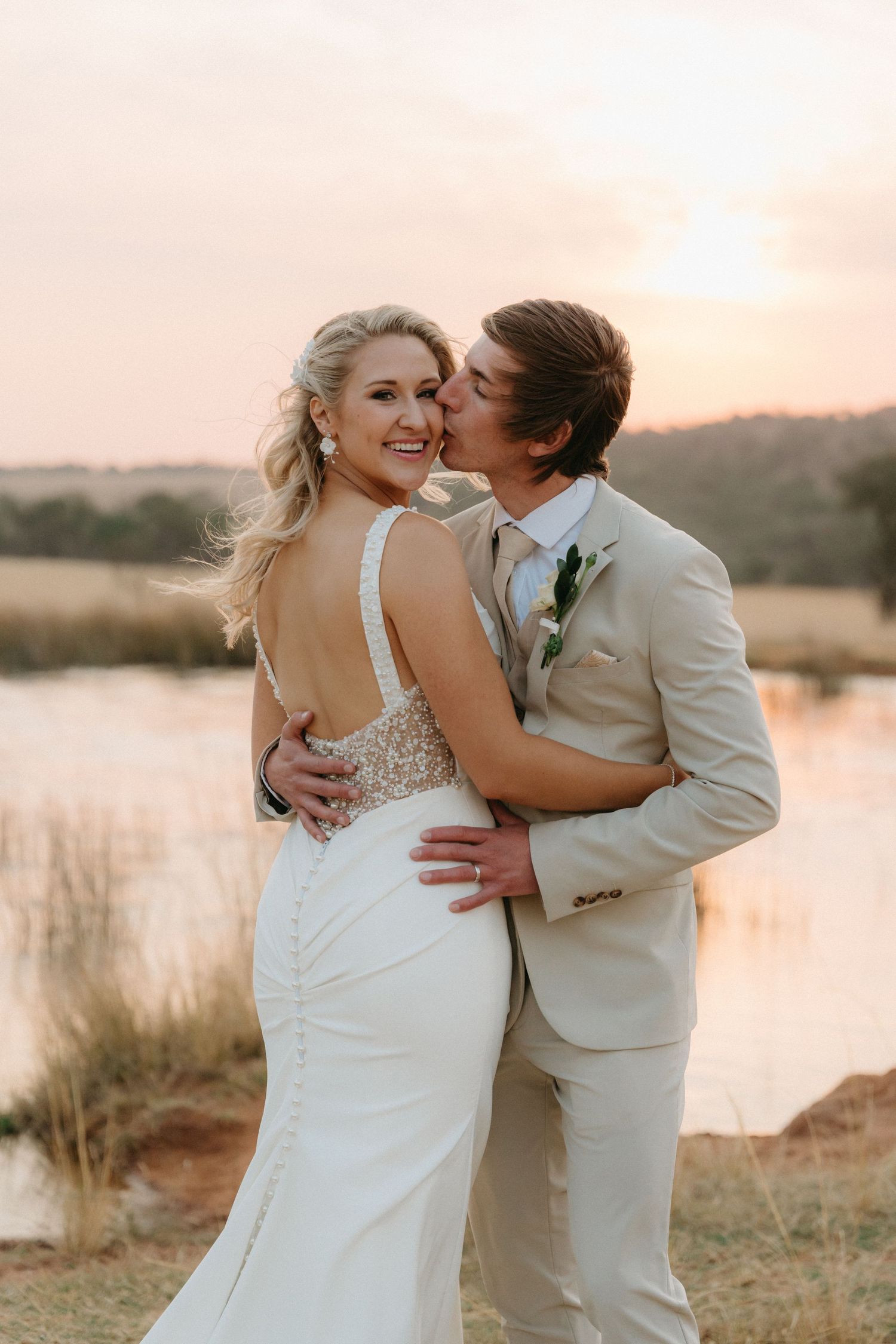 Romantic sunset portrait of a couple in wedding attire by a lake.