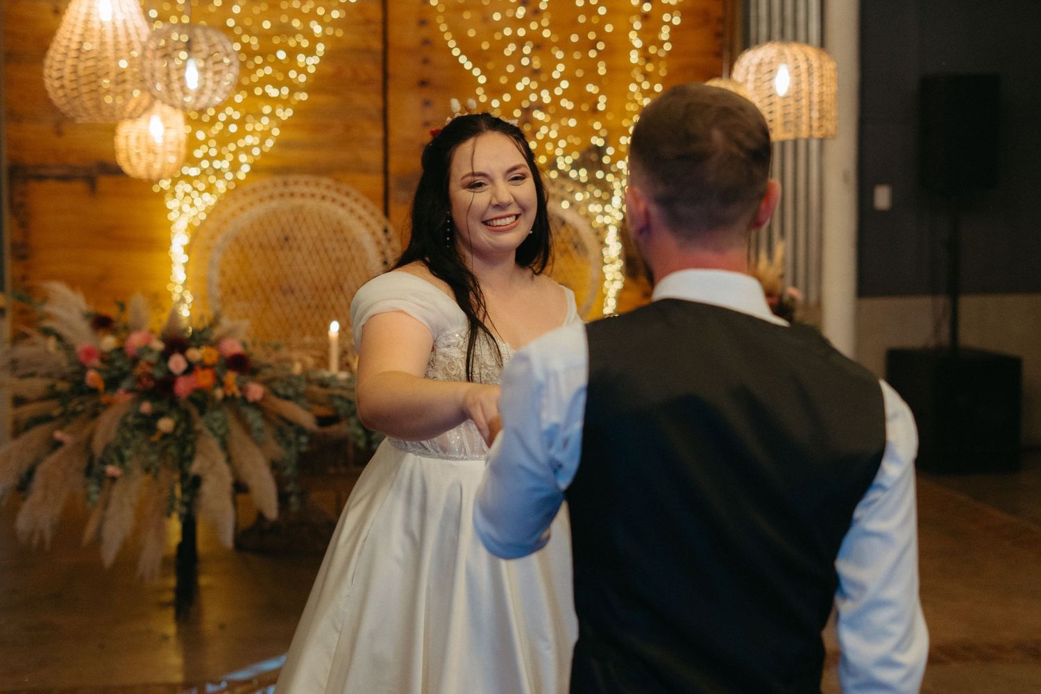 A rustic barn wedding reception venue with string lights and a boho peacock chair backdrop.