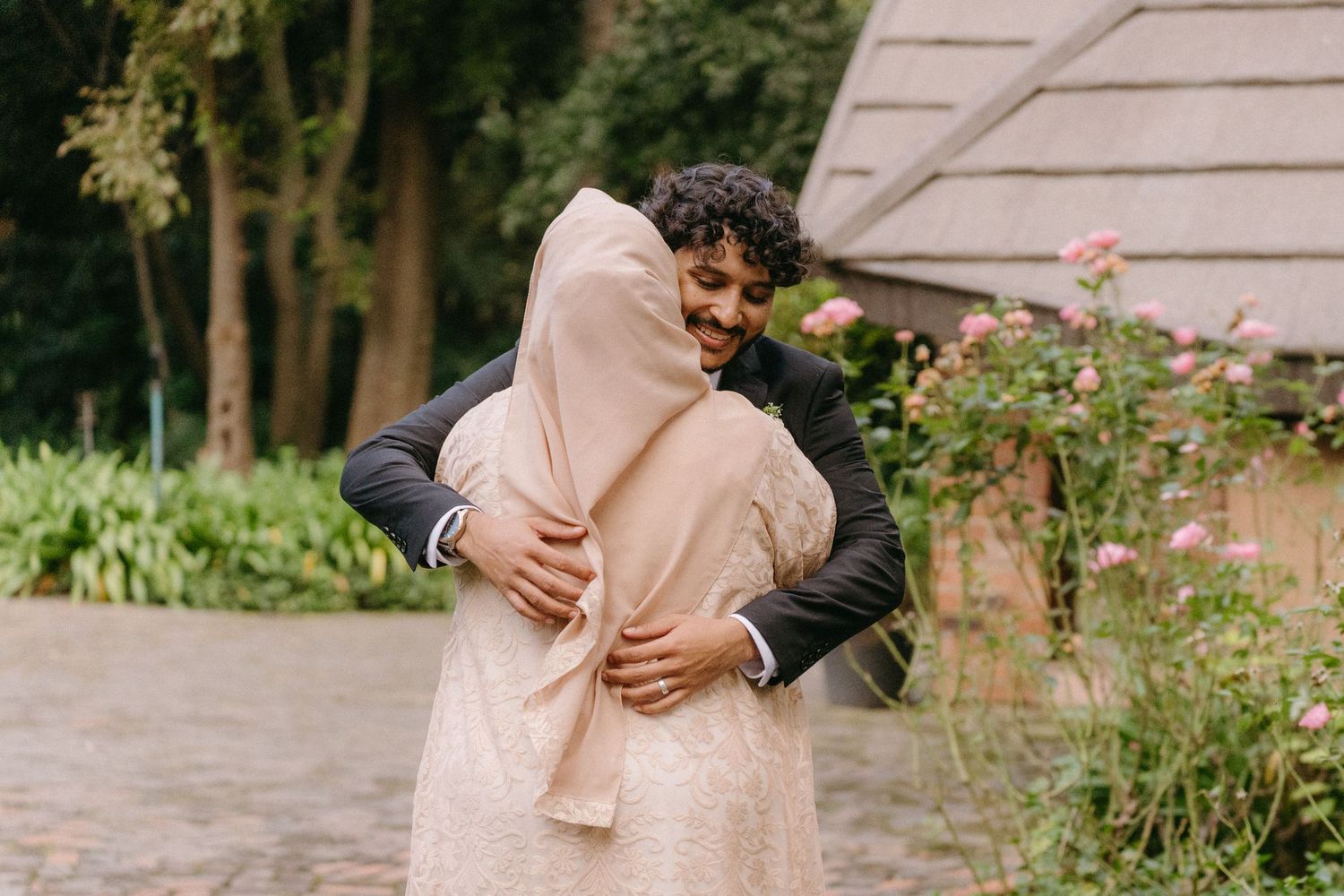 Joyful embrace between wedding couple amid garden greenery and architecture.