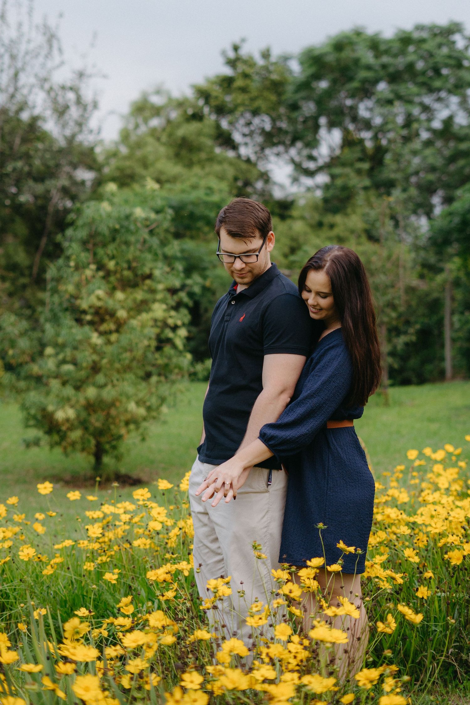 A couple embraces while standing in a meadow filled with vibrant yellow wildflowers on a spring day.