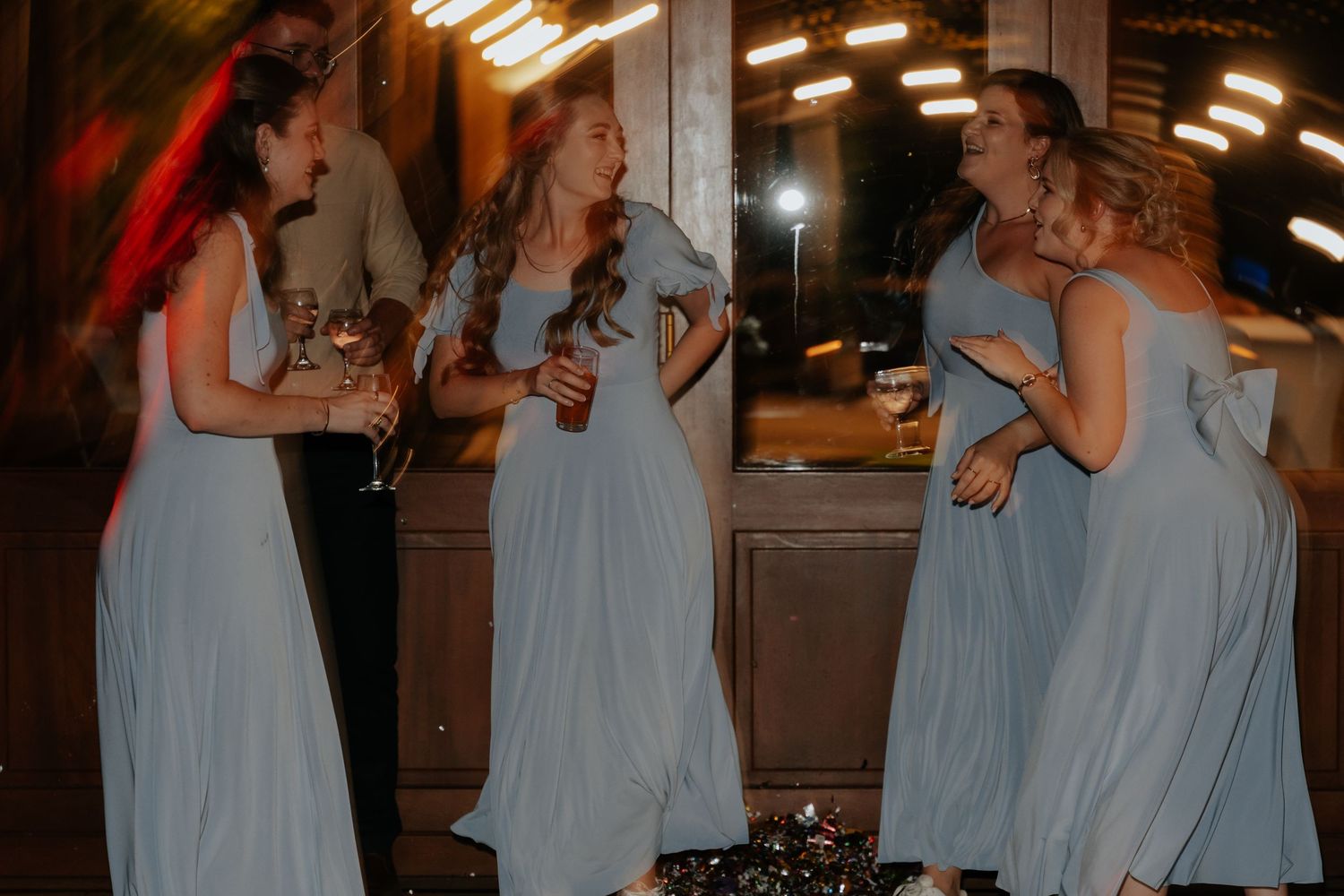 Bridesmaids in pale blue dresses enjoying drinks and dancing at a wedding reception.