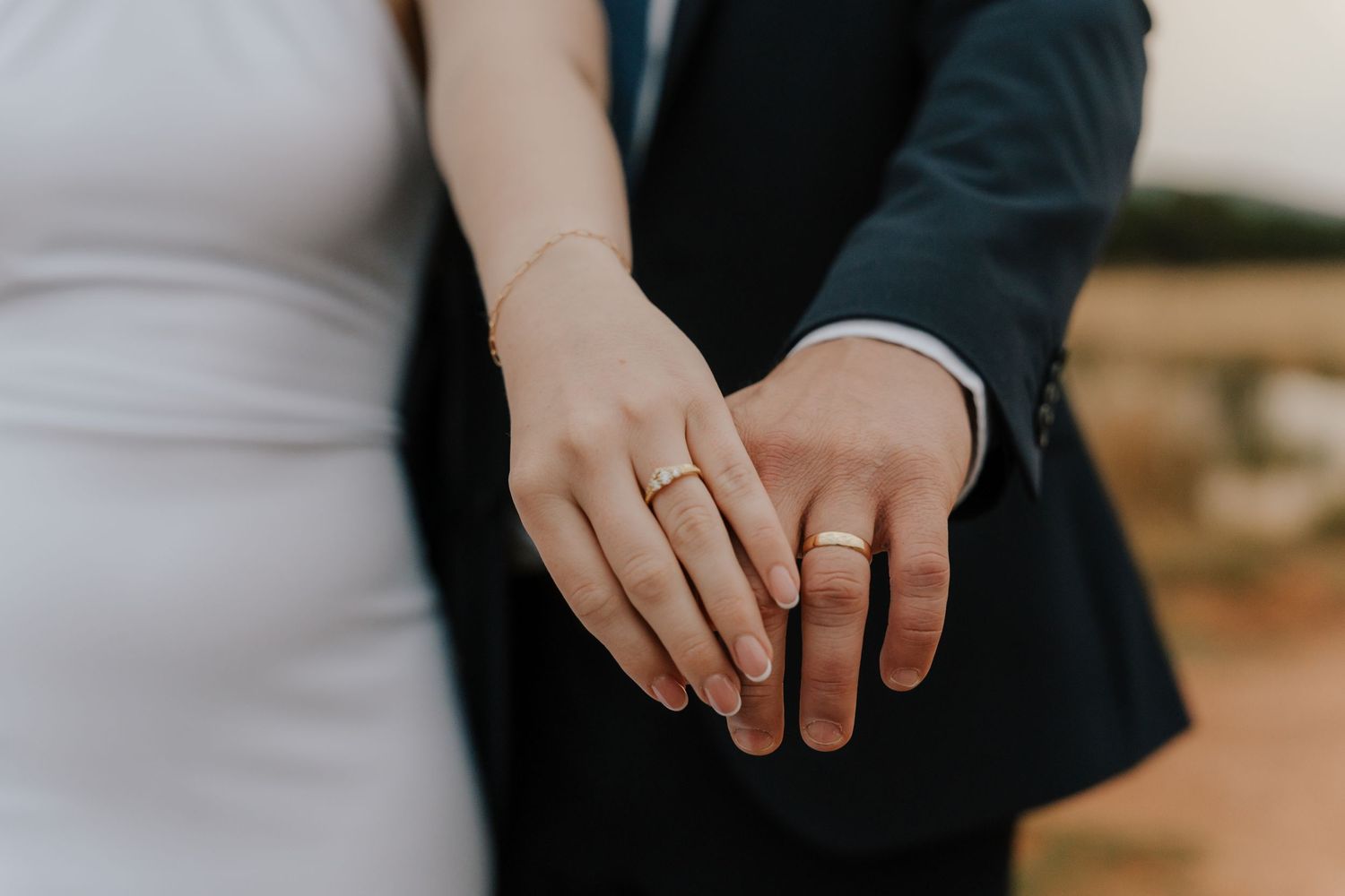 A person wearing a black suit and white shirt holds their hands together in front of them.