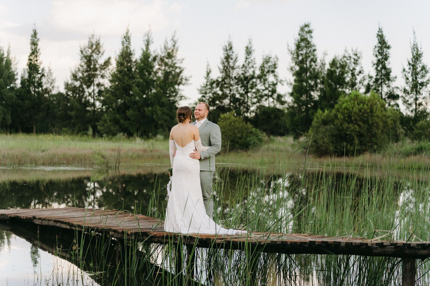 A couple shares an intimate moment on a rustic wooden dock surrounded by lush greenery and still waters.