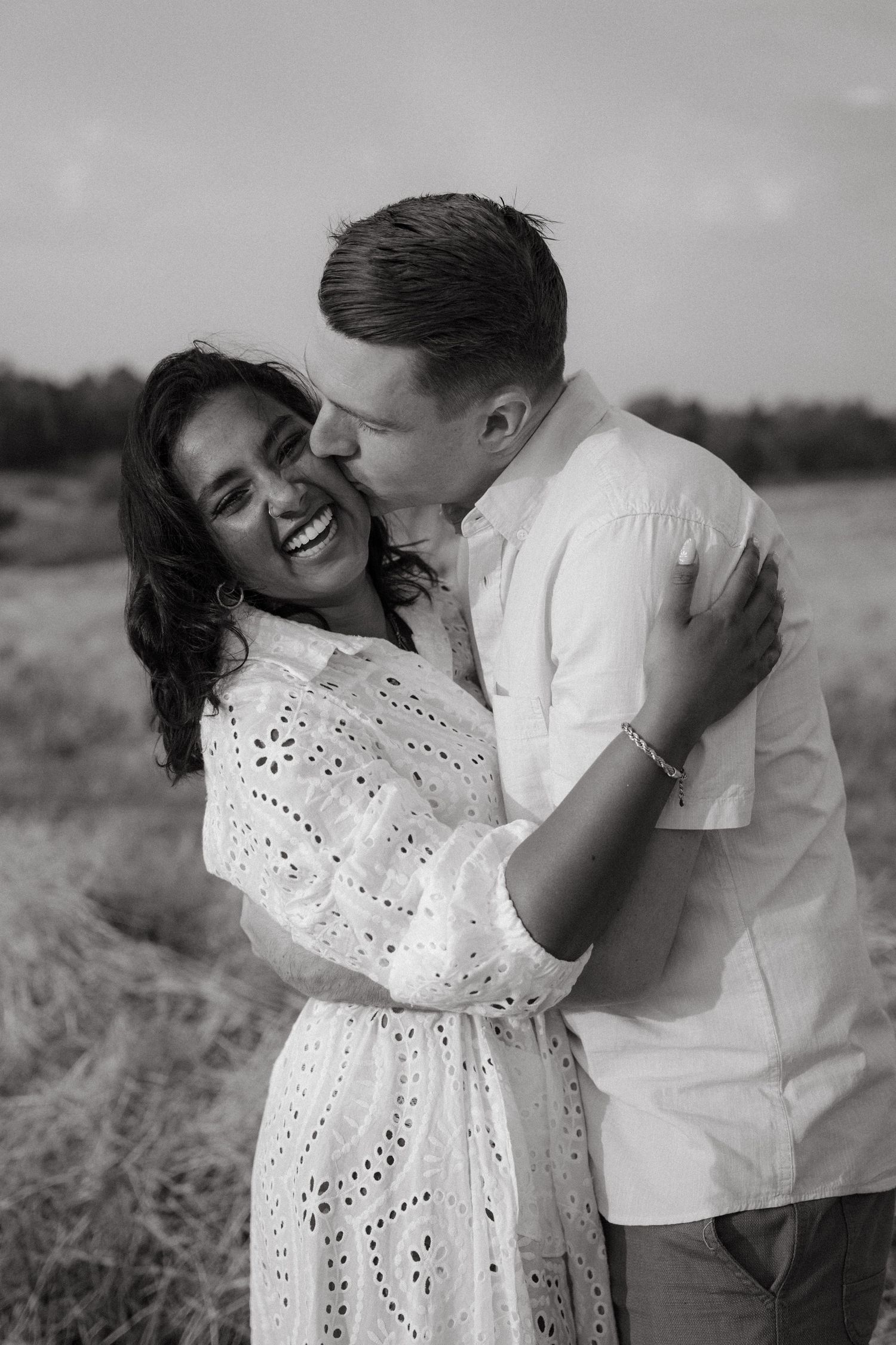 Black and white photo of a couple sharing intimate moments and laughter in an outdoor setting.