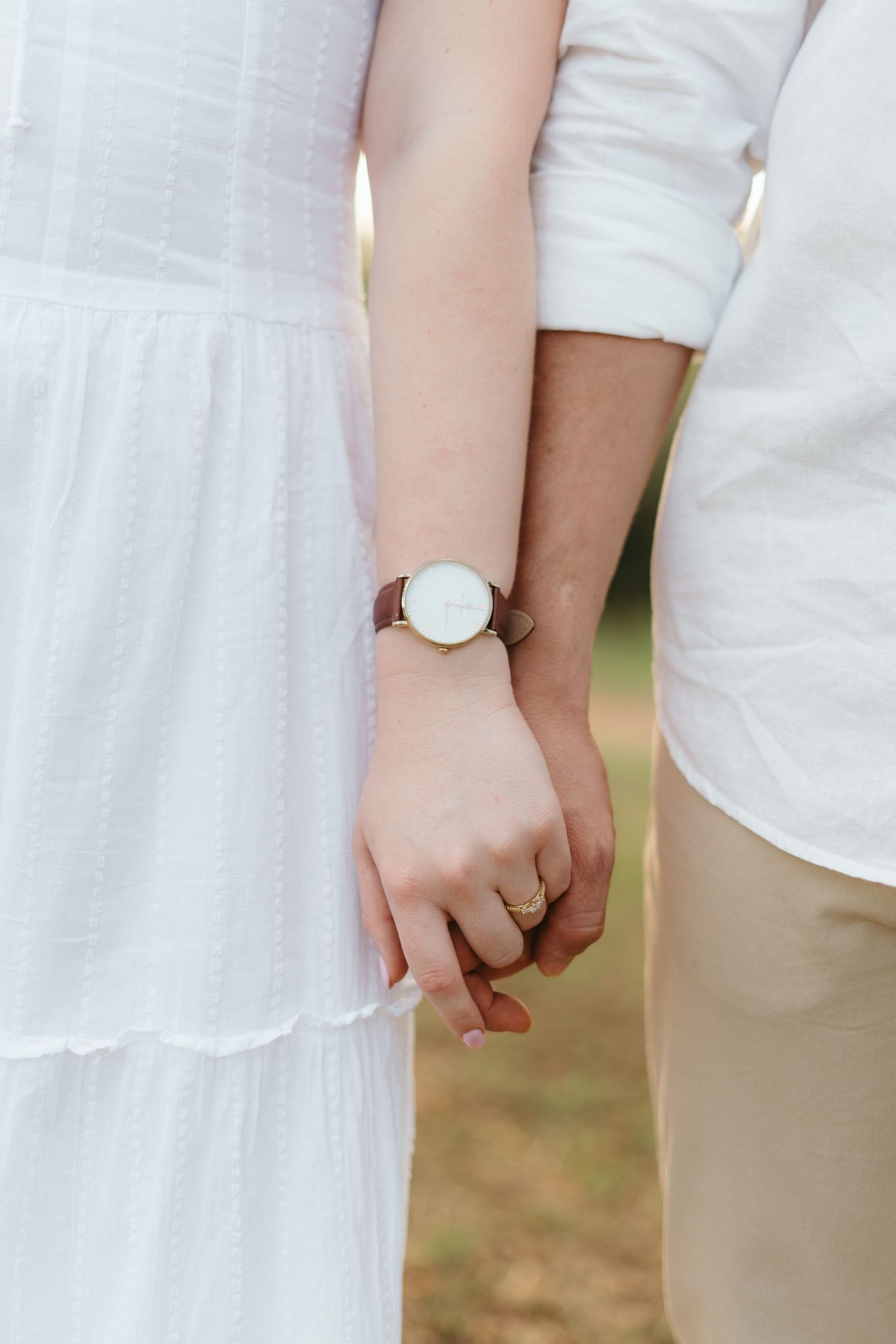Close-up of hands wearing matching white and brown minimalist watches against white clothing.