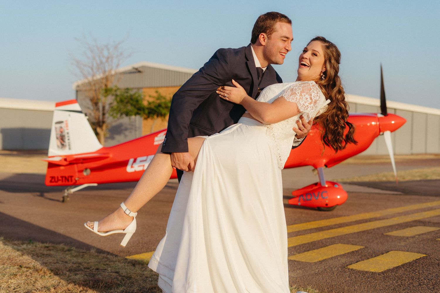A playful wedding photo with a vintage red airplane in the background.