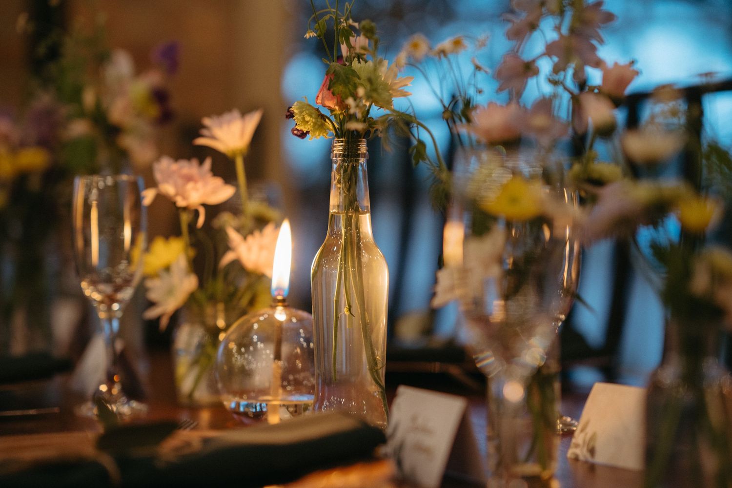 Elegant wedding reception table setting with wine bottle centerpiece and candlelight.
