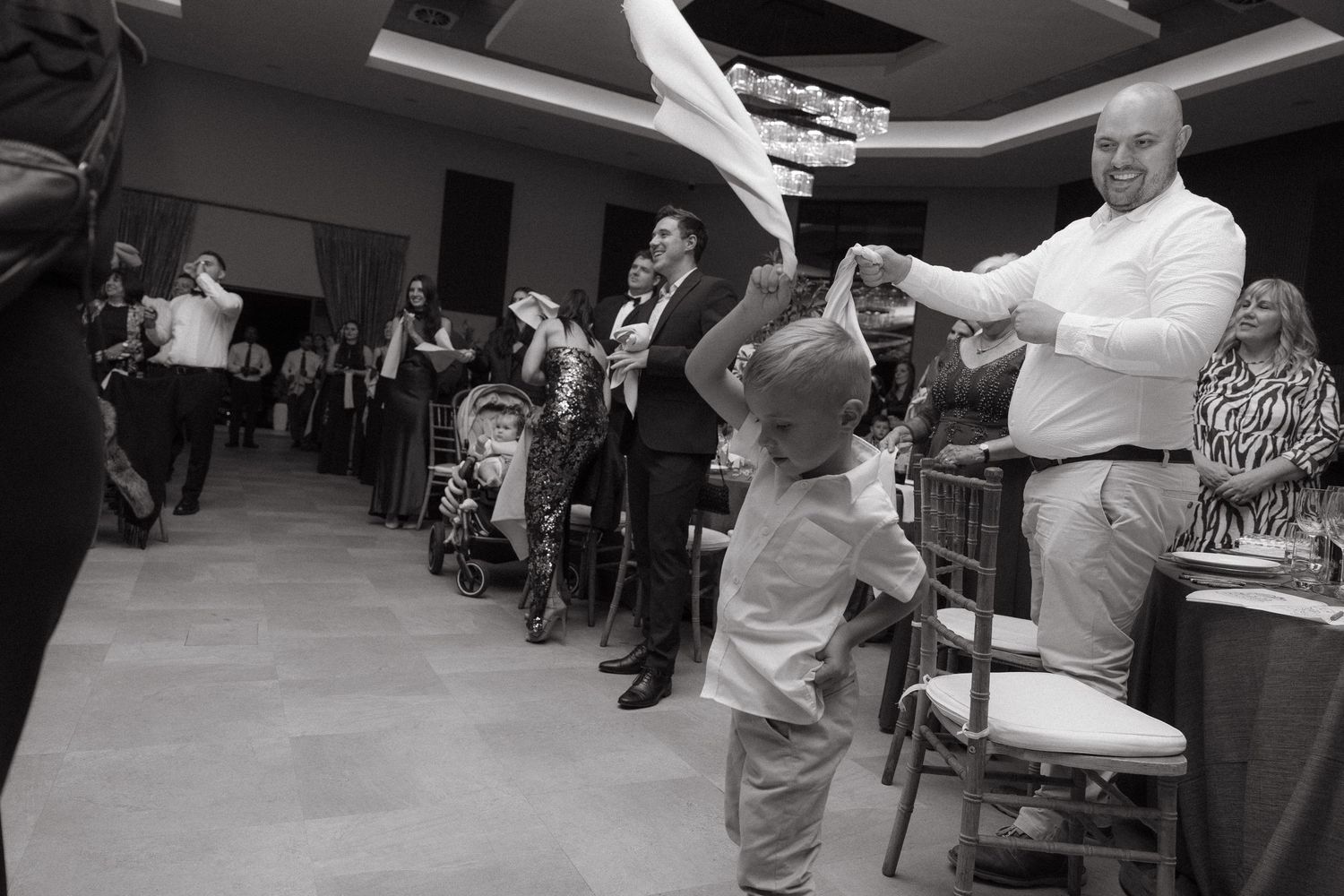 Black and white photo of adults and a child dancing joyfully at an elegant wedding reception celebration.