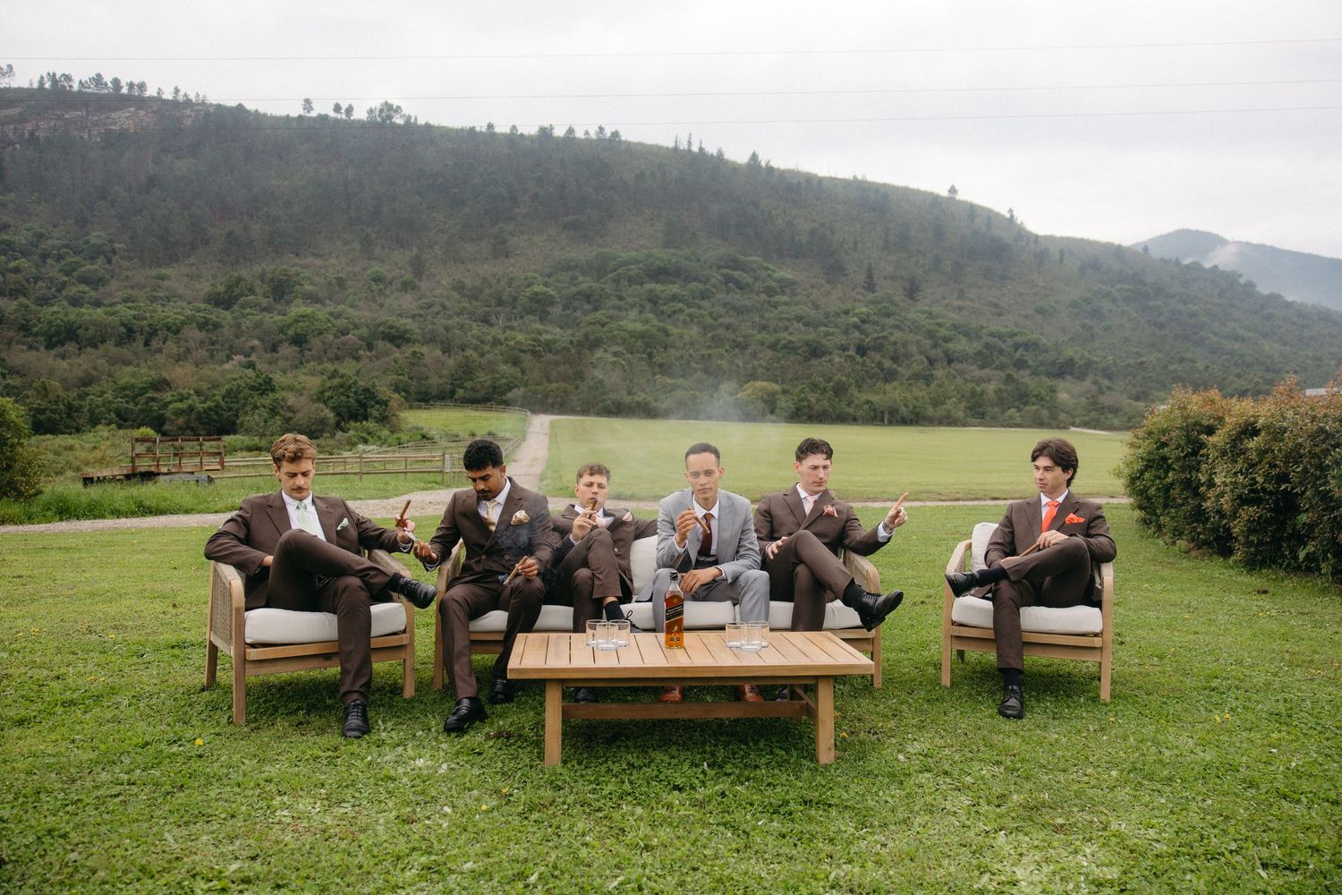 Groomsmen in brown suits relaxing on outdoor furniture with mountain backdrop at a scenic wedding venue in the Garden Route.
