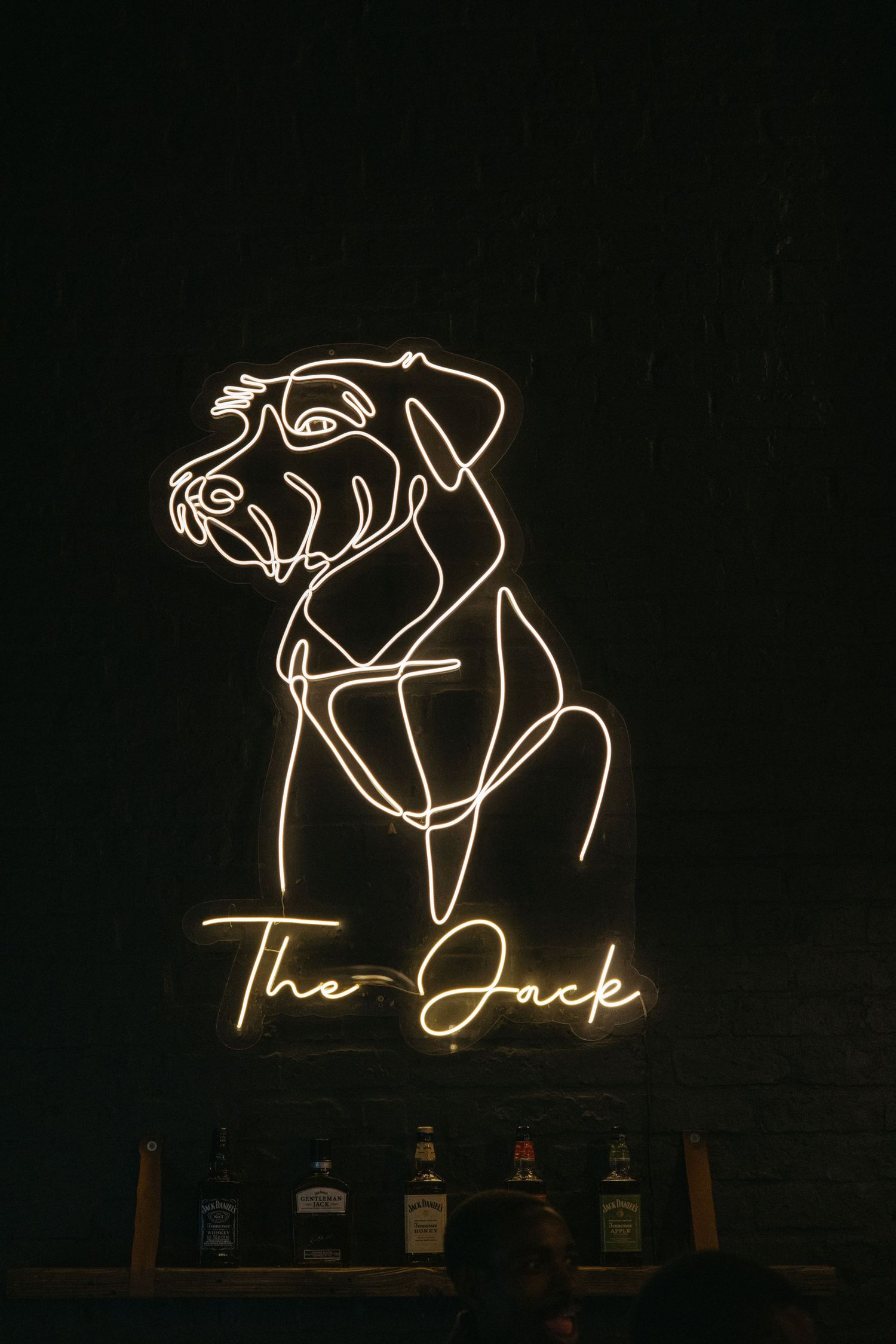 Illuminated neon dog outline sign with 'The Jack' text displayed above bottles on a dark background.