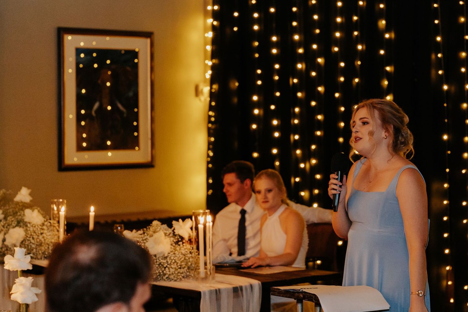 Wedding reception tables decorated with white linens, candles and twinkle lights creating a warm, romantic ambiance.