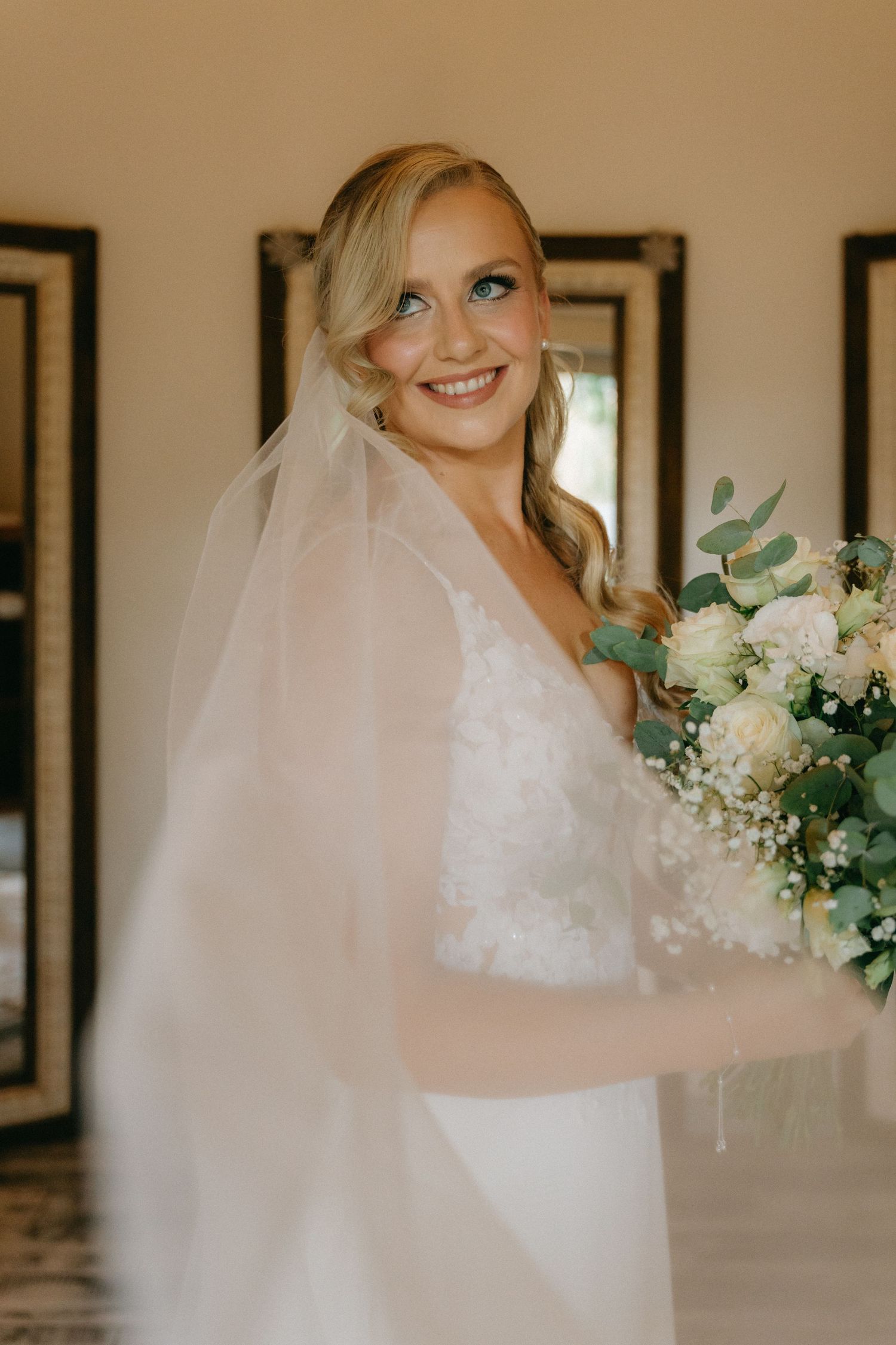 Bridal portrait in an elegant white gown with delicate veil and white floral bouquet.