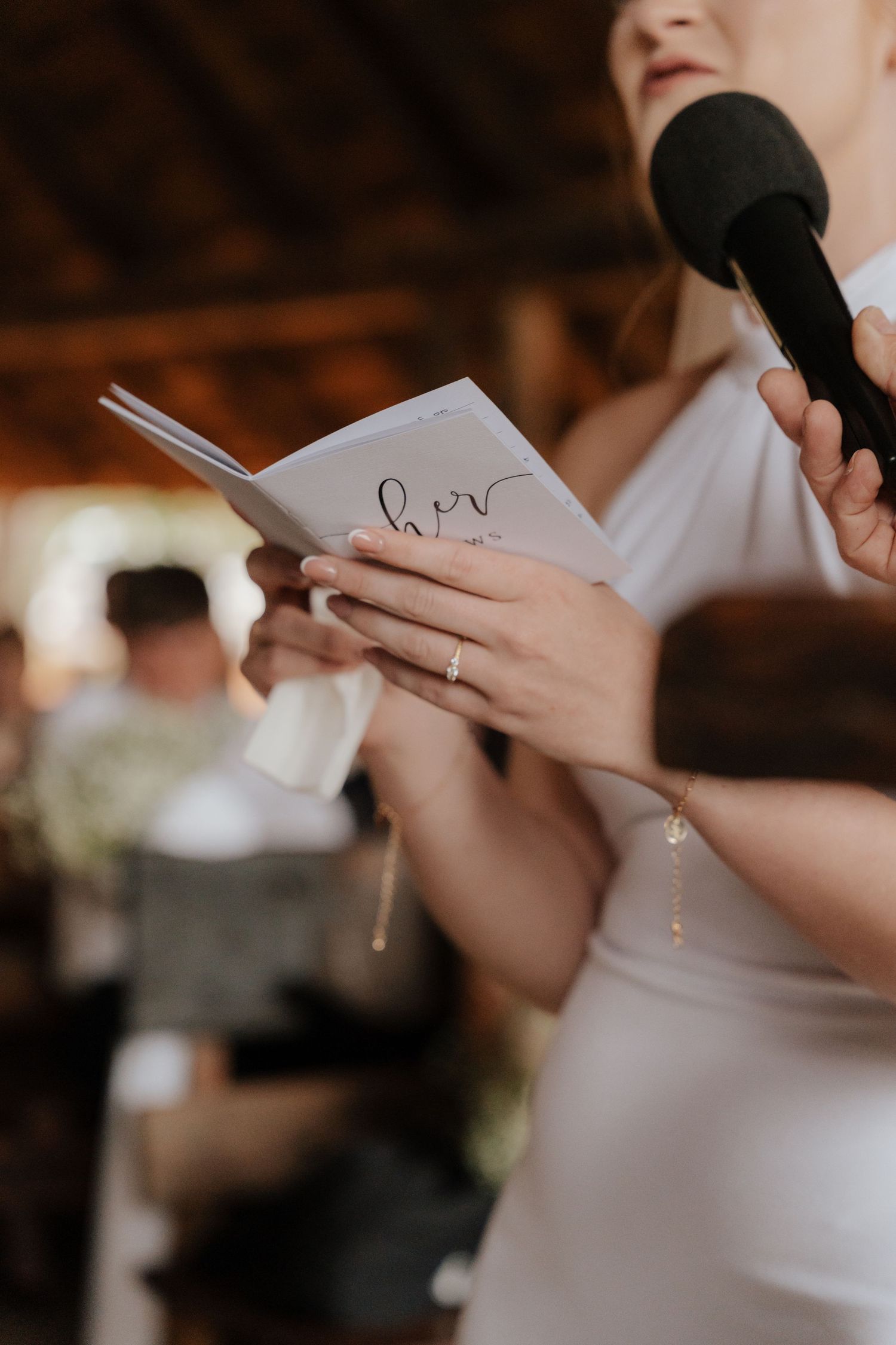 Close up of hands holding a microphone and reading from a vows booklet during a wedding ceremony.