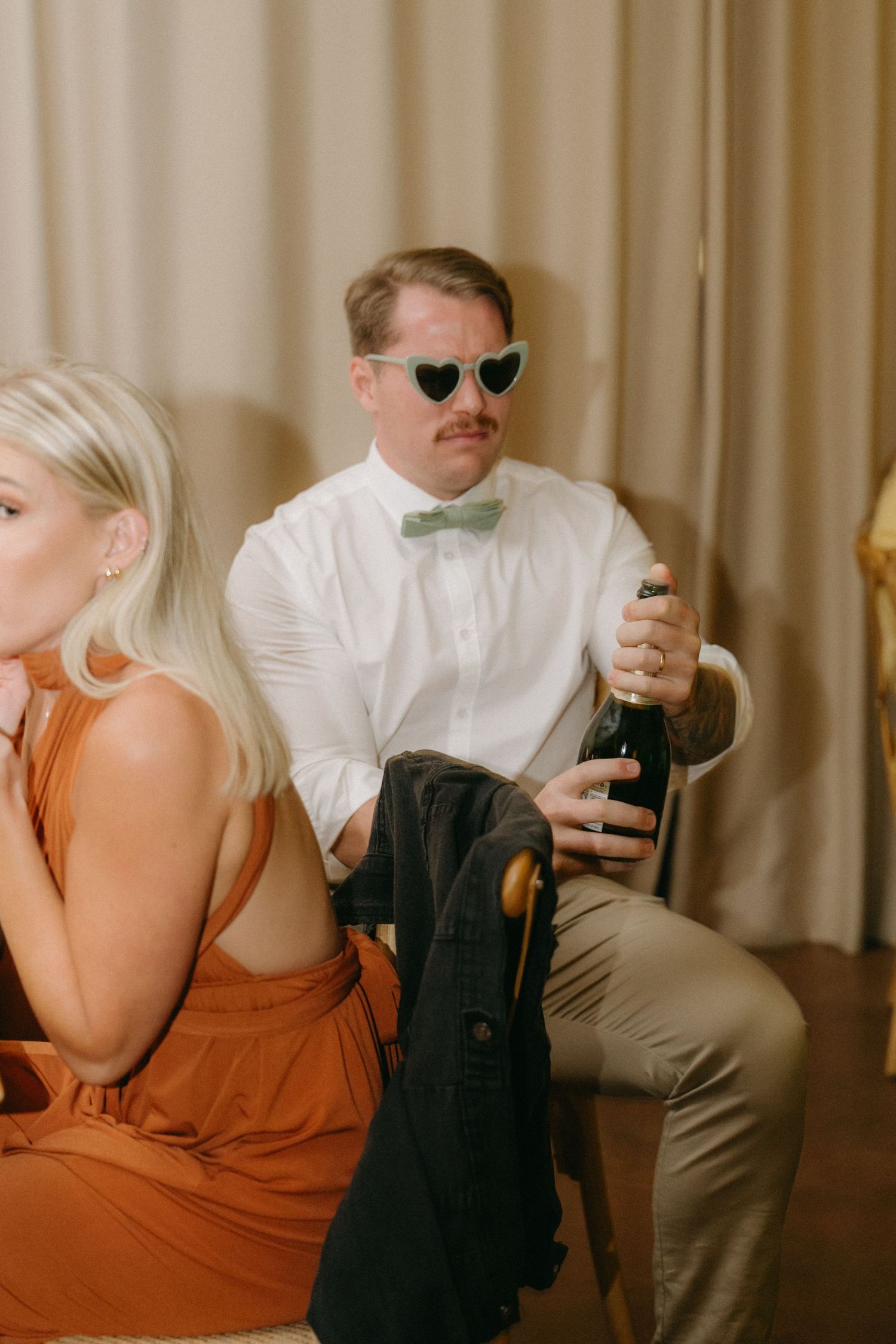 Wedding party members in orange dresses and formal attire share candid moments at a reception.