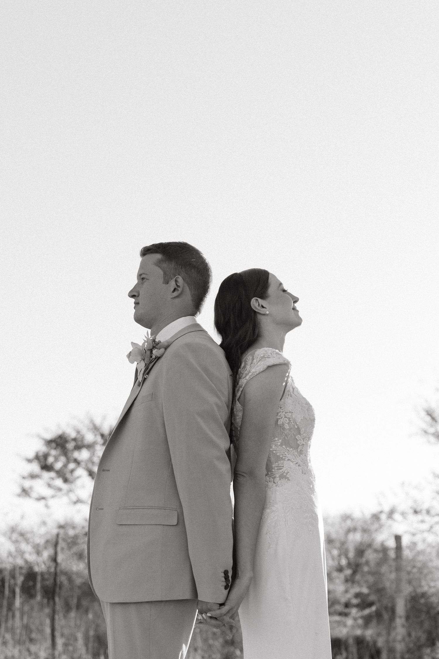 A black and white artistic portrait of newlyweds standing back to back outdoors.