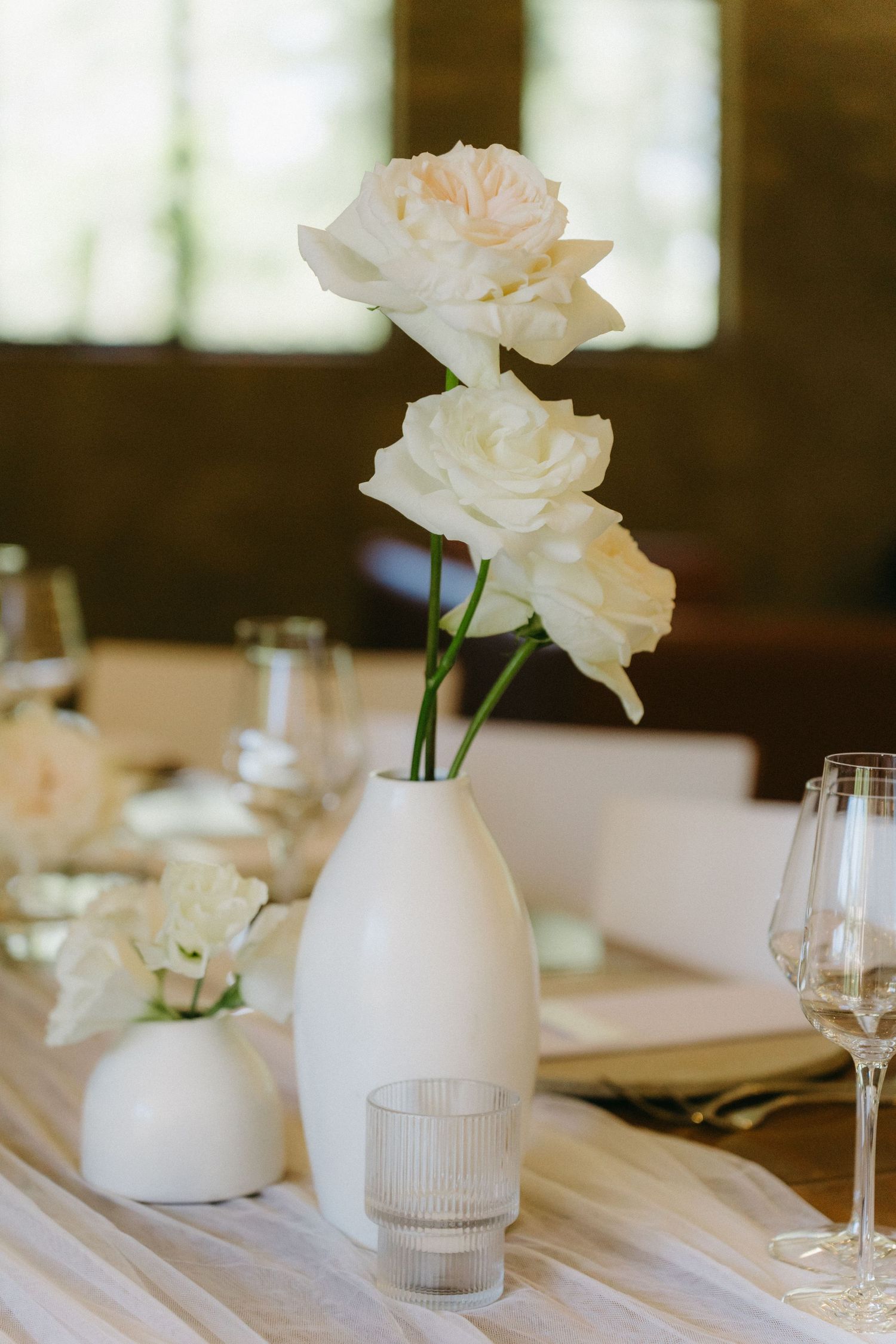Elegant white roses in a modern vase with wine glass on wedding reception table.