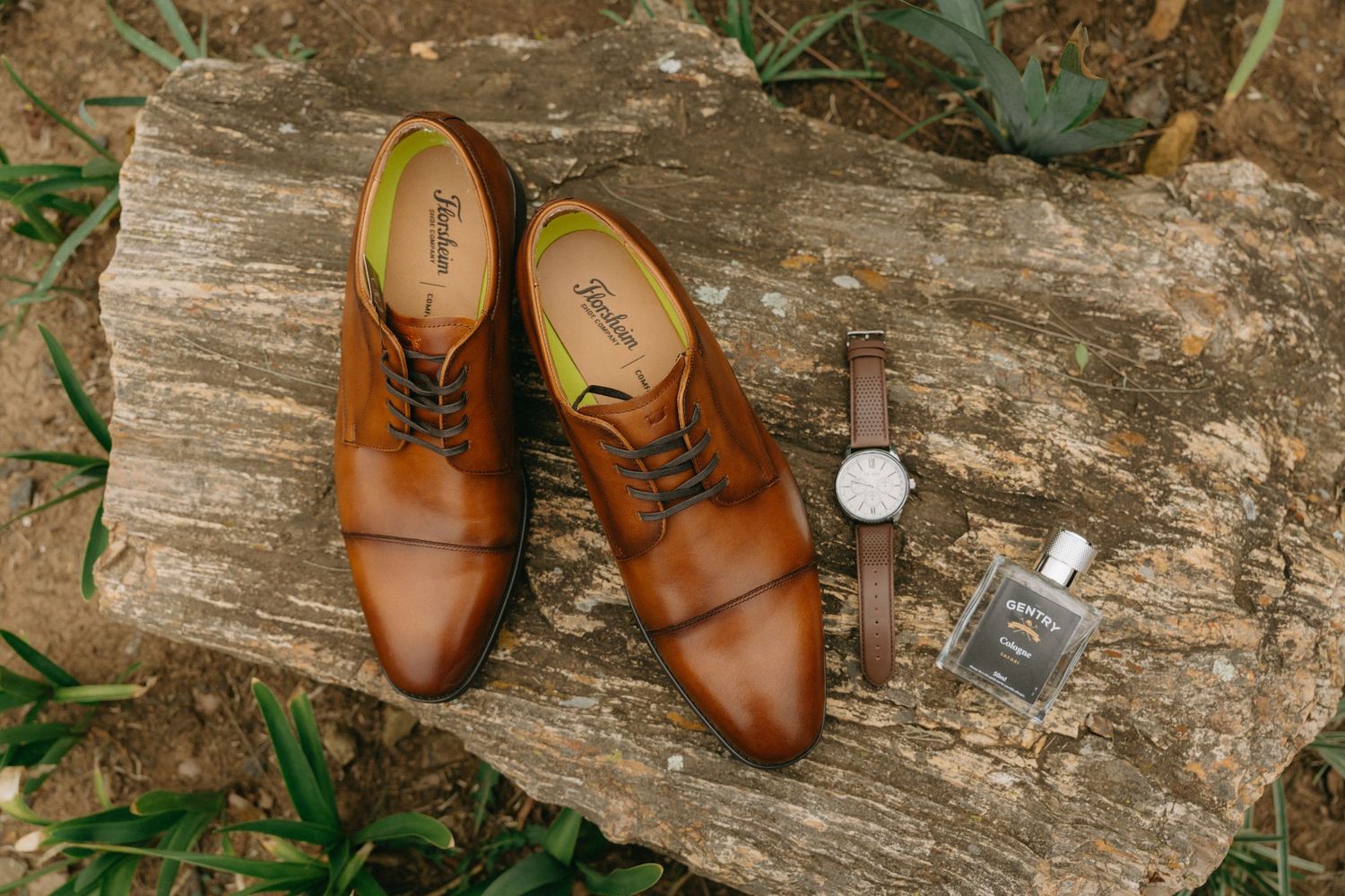 Brown leather dress shoes arranged on rustic wooden log for wedding detail photography.
