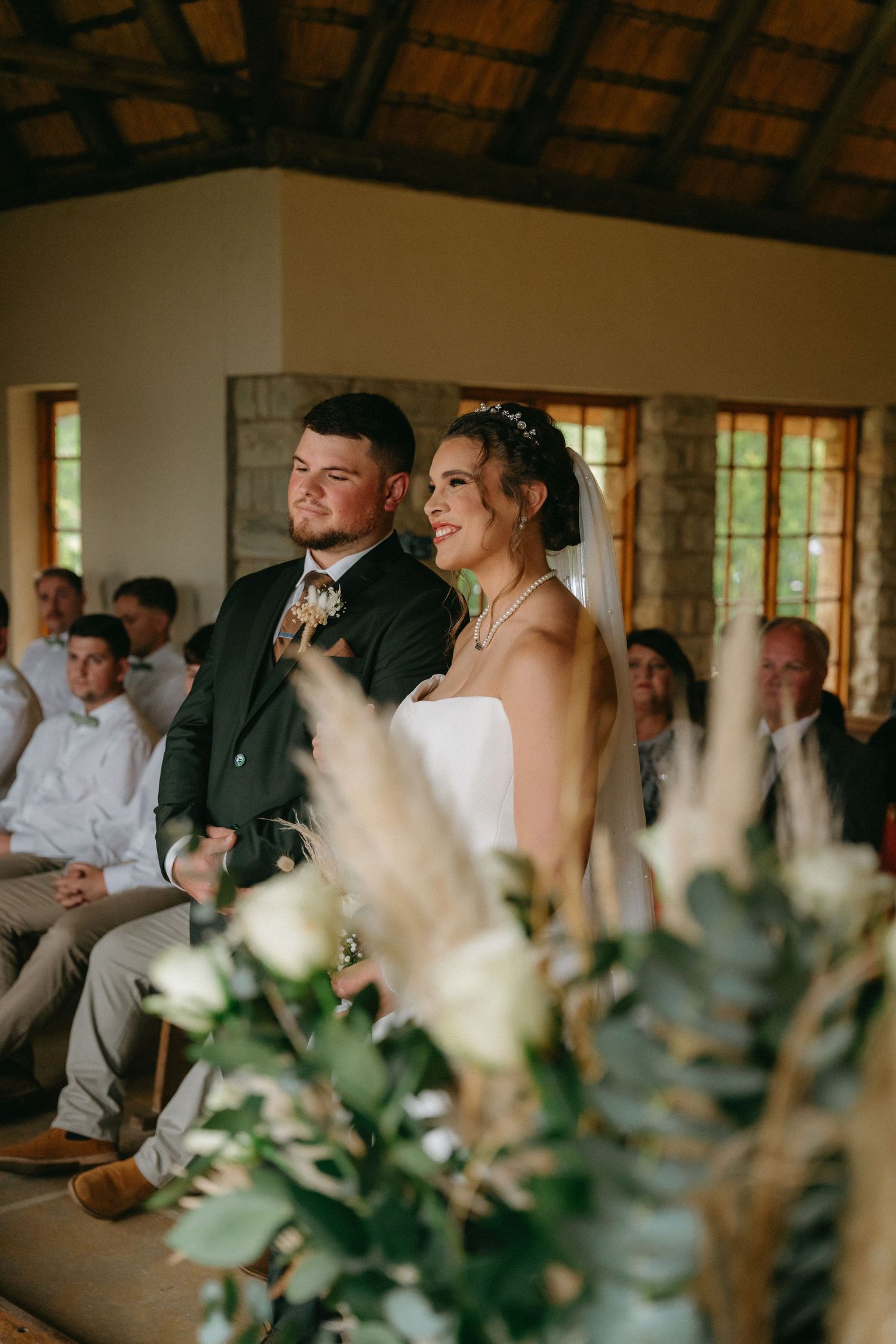 Wedding guests laugh and smile during an indoor reception with white floral centerpieces on tables.