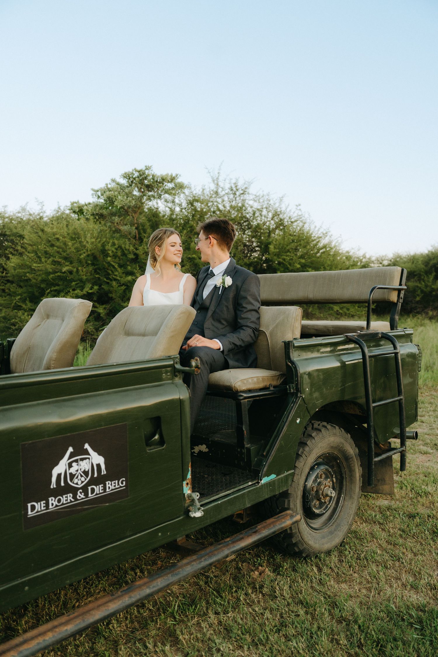 A couple sits together in a vintage green Land Rover during their wedding photoshoot.