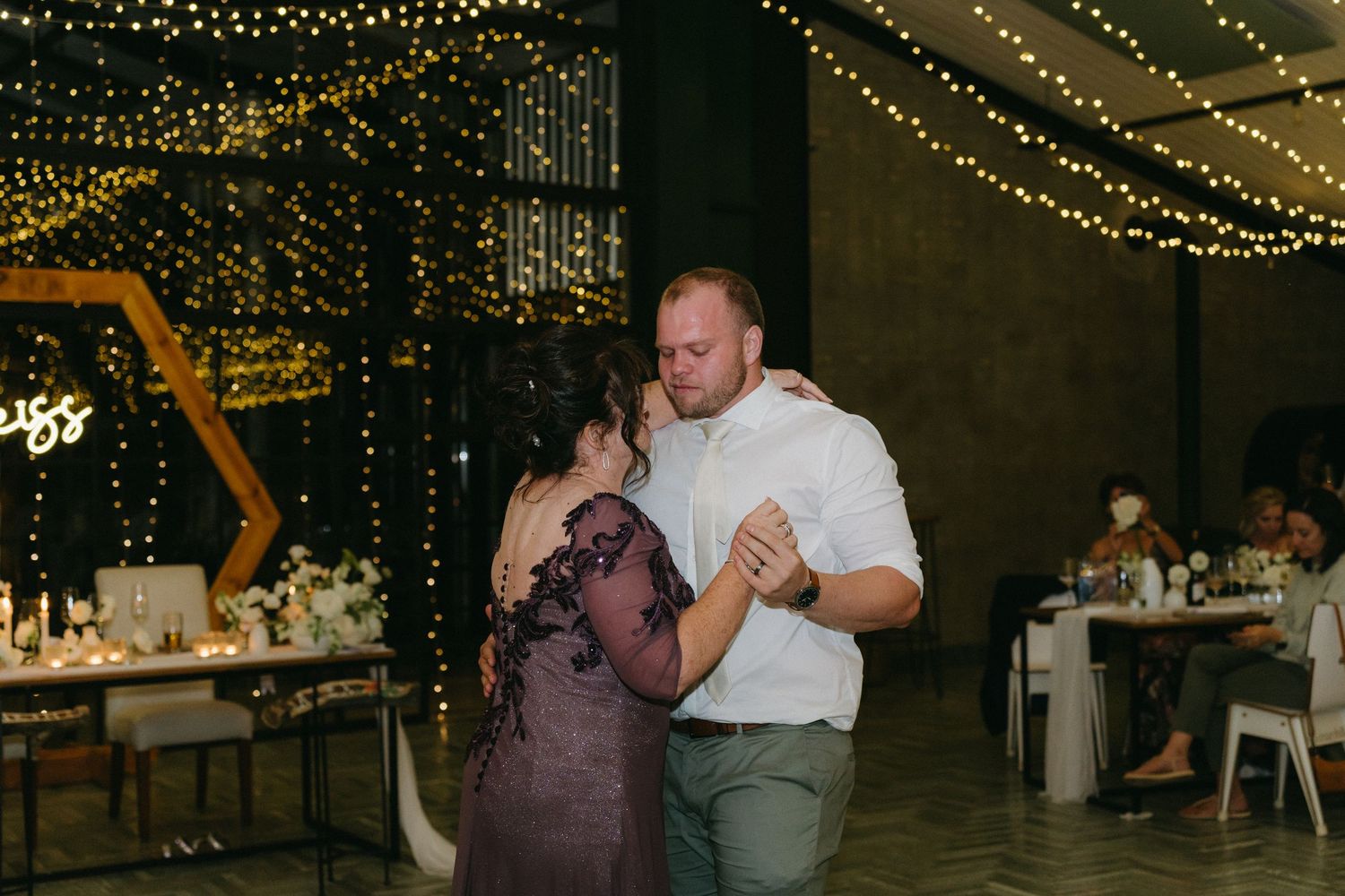 Couple dancing together at dimly lit reception venue with string lights overhead.