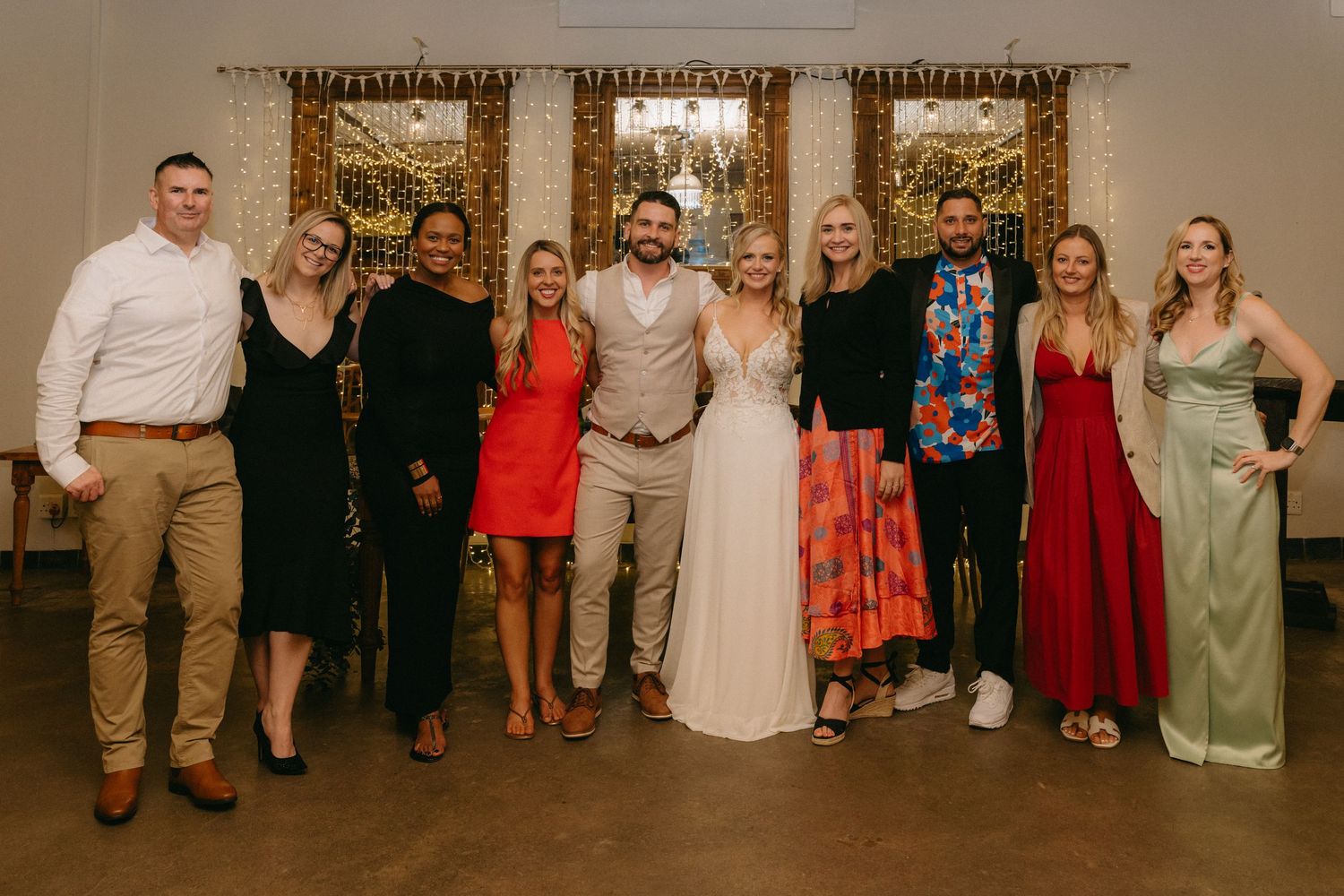 Wedding guests gather for a group photo in an indoor venue with decorative lighting.