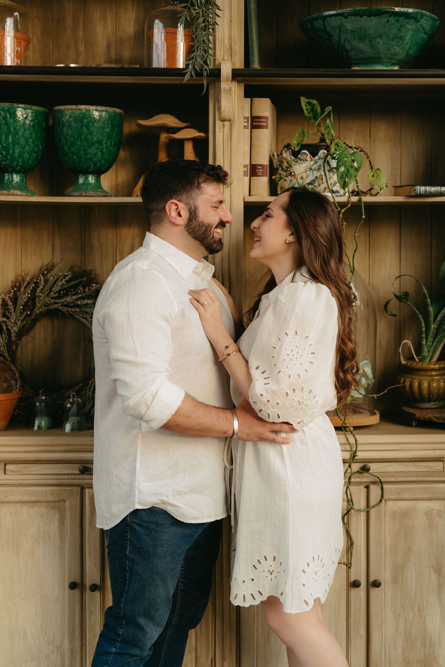 Romantic couple shares intimate moments in kitchen with white cabinets and houseplants in background.