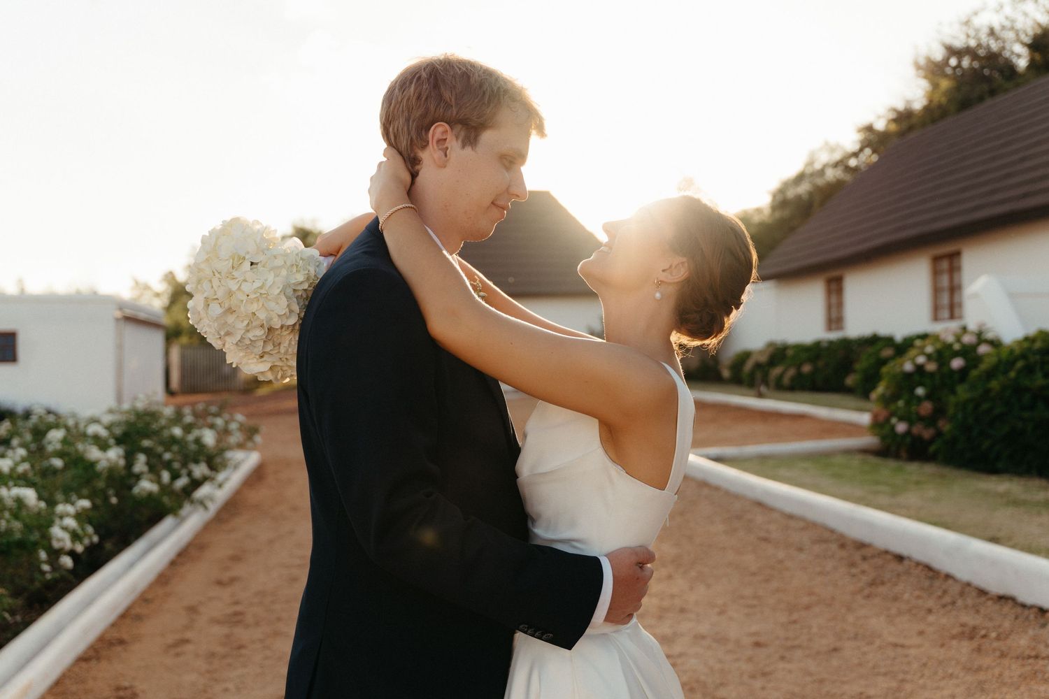 A couple shares a romantic sunset kiss on their wedding day in a rustic outdoor setting.