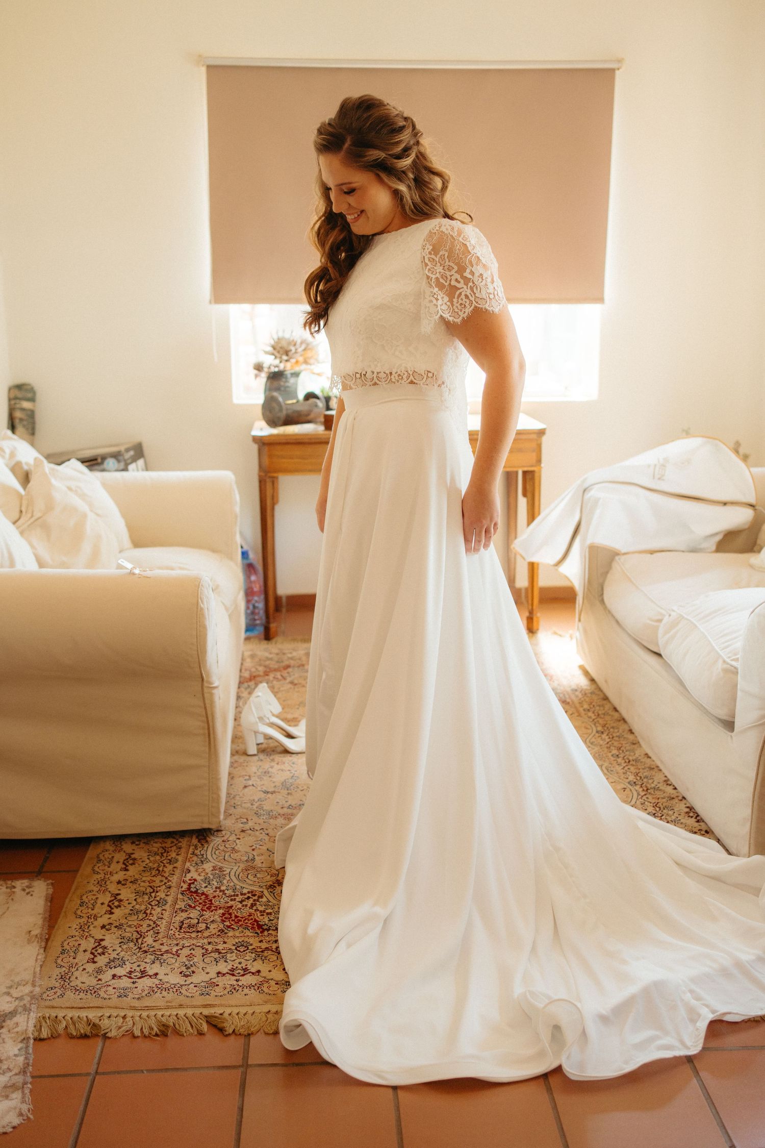 A flowing white wedding gown with lace details and train photographed in a cozy living room setting.