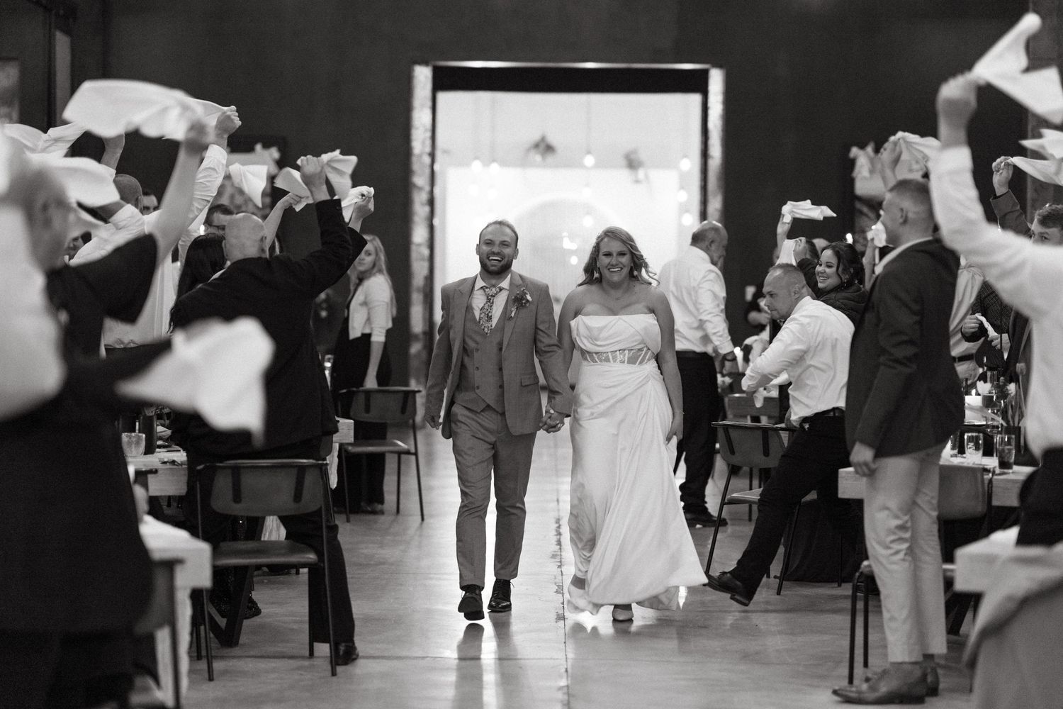 A black and white wedding photo shows a couple walking down the aisle while guests wave streamers and handkerchiefs.