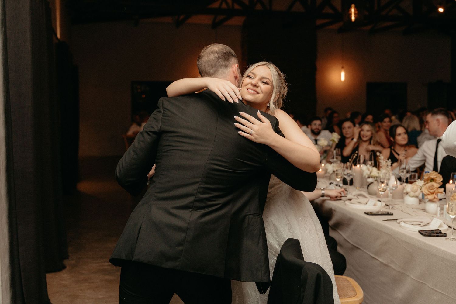 Wedding guests dancing together at an evening reception with dining tables and candlelight in the background.