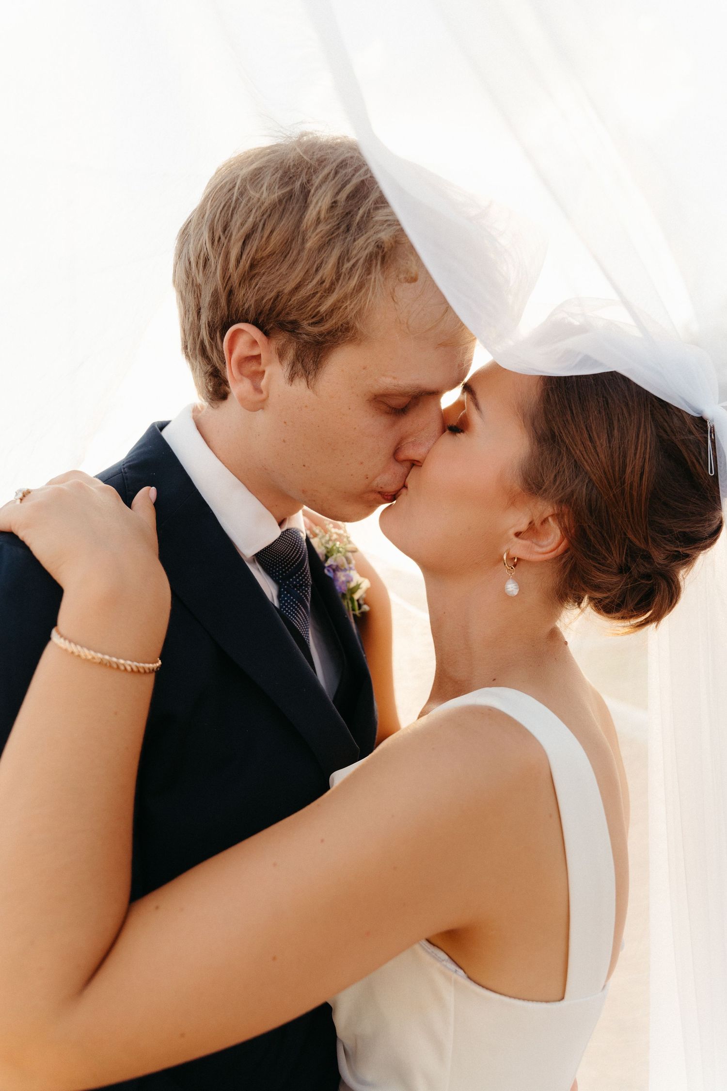 Three romantic wedding photos show tender kisses between newlyweds in white dress and black suit against bright background.