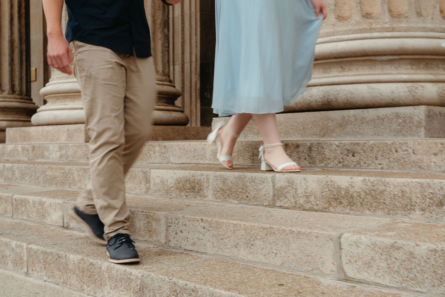 A person in khaki pants and blue shirt walks down stone steps at a historic building entrance.