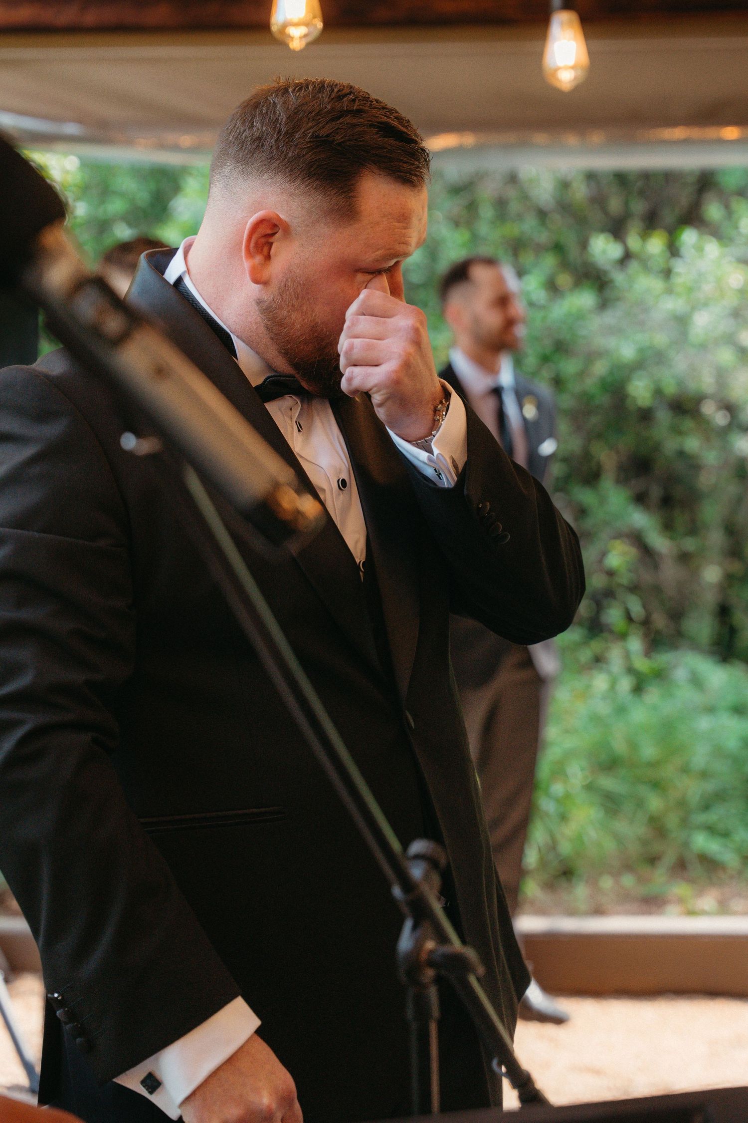 Emotional moments captured at a wedding ceremony as someone wipes away tears while wearing a black suit.