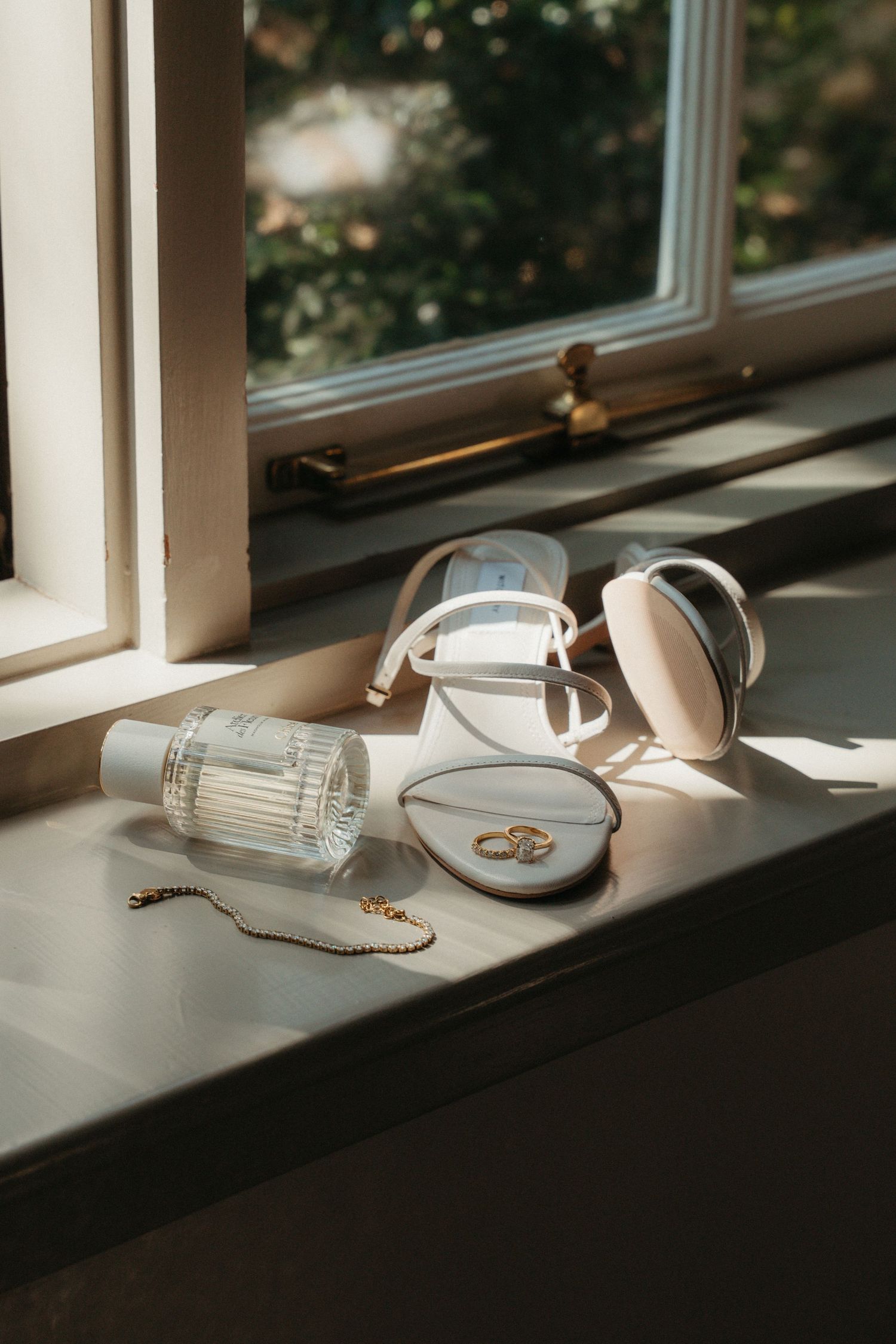 Bridal accessories including white sandals, perfume, sunglasses, and gold rings on sunny windowsill of Beechwood Gardens
