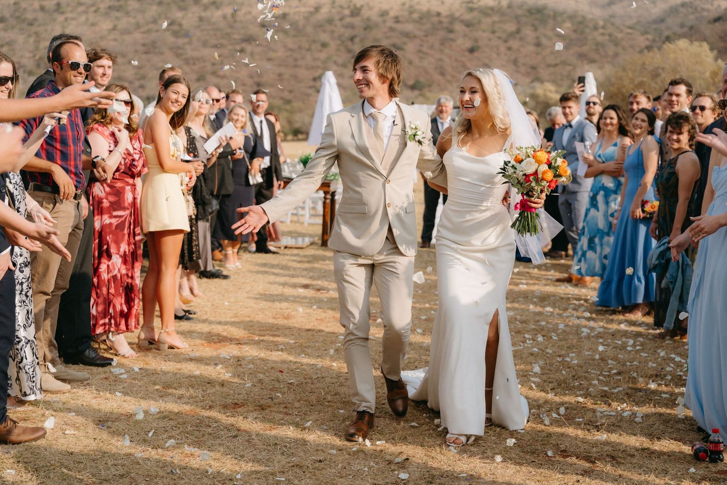 A wedding ceremony takes place in a scenic desert landscape with guests watching the couple exchange vows.