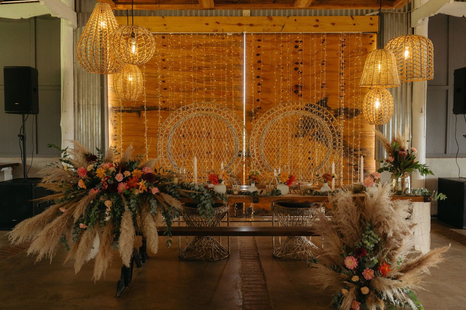 Modern rustic wedding reception decor with hanging lights and dried pampas grass floral arrangements.