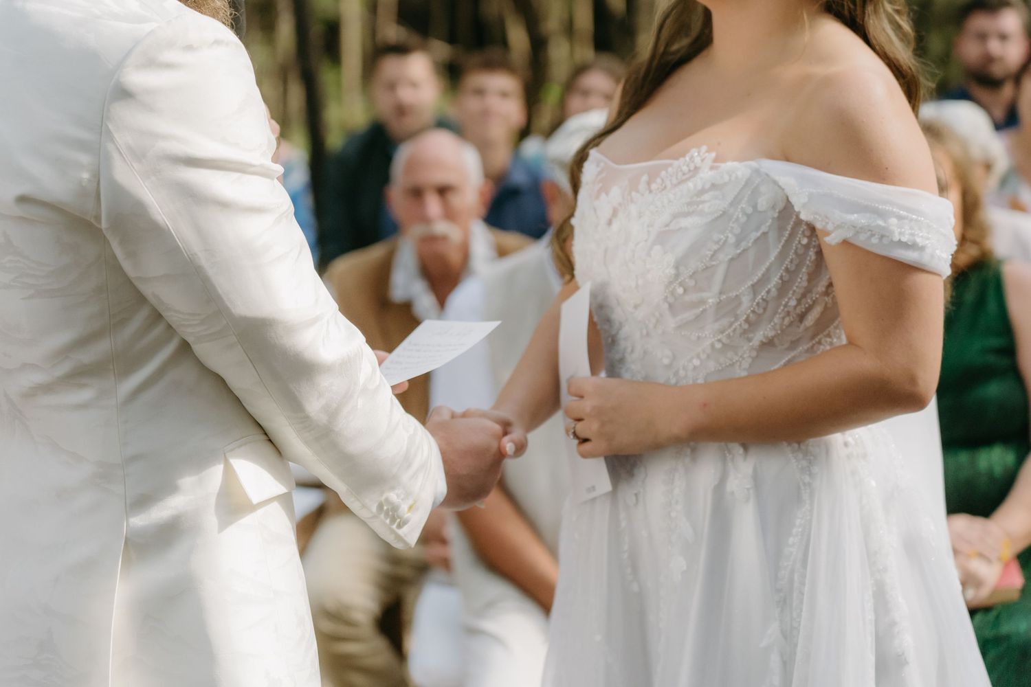 Close-up view of a couple exchanging rings during a wedding ceremony, with the bride wearing an off-shoulder white dress.