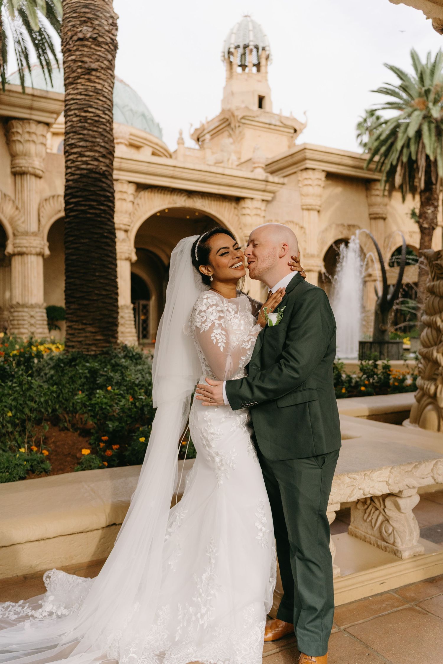 A couple shares romantic moments at a luxurious venue with Mediterranean architecture and palm trees.