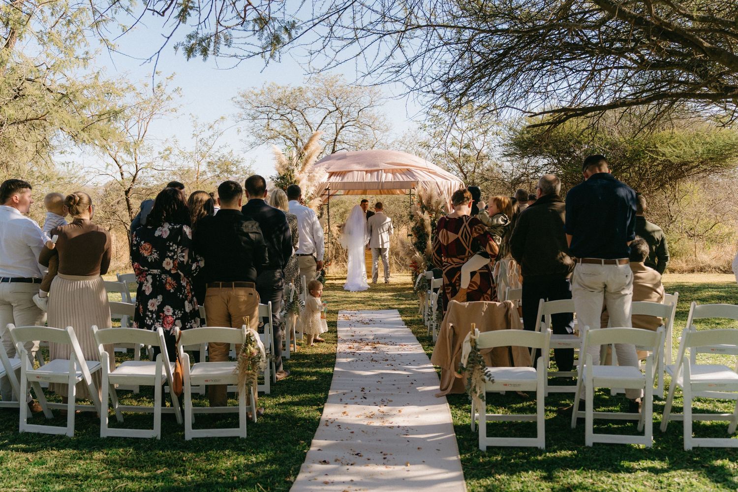 White chairs line an outdoor wedding ceremony aisle under bare winter trees.