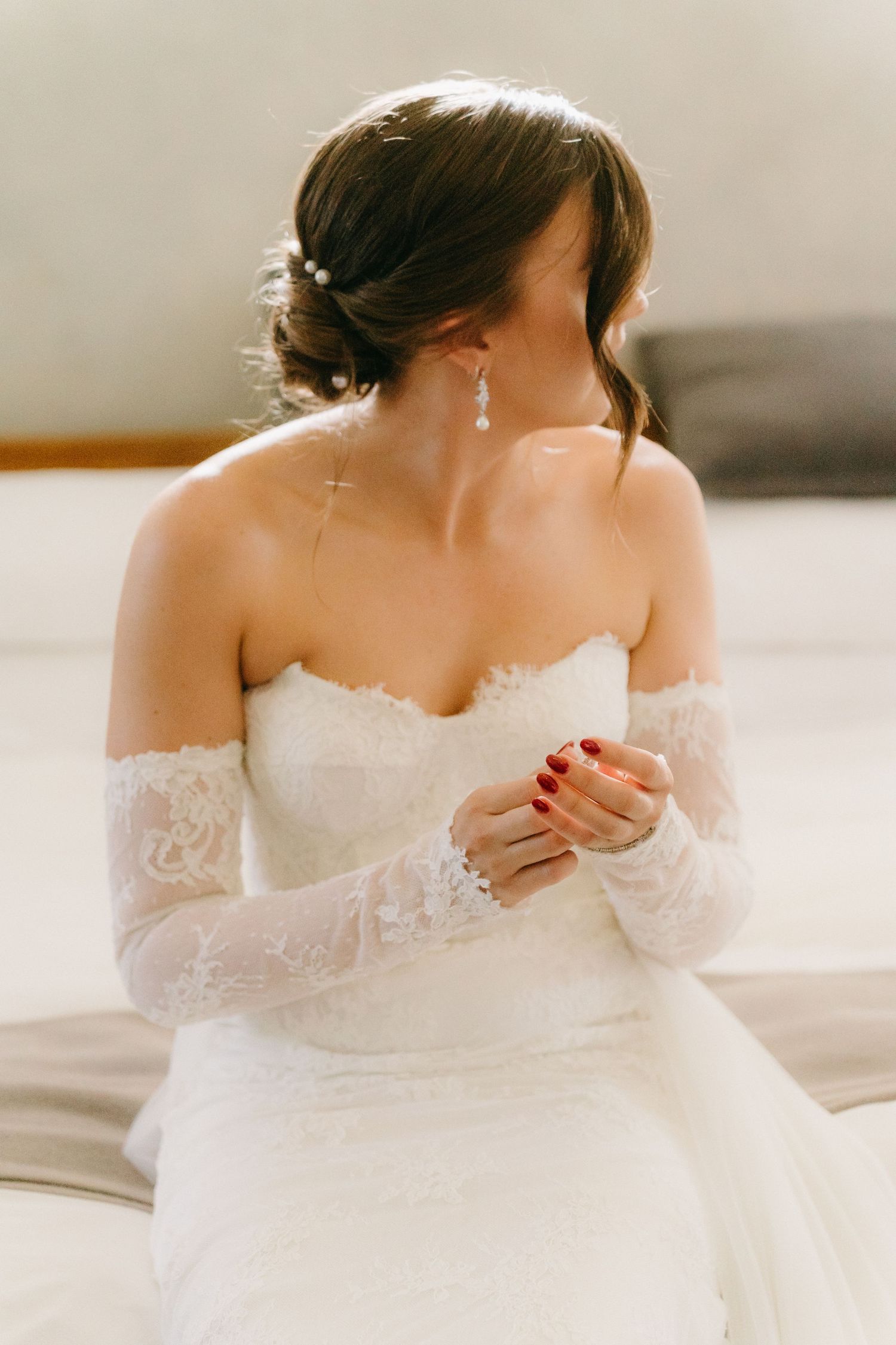 Side view of bride in off-shoulder lace wedding gown with elegant updo and earrings.