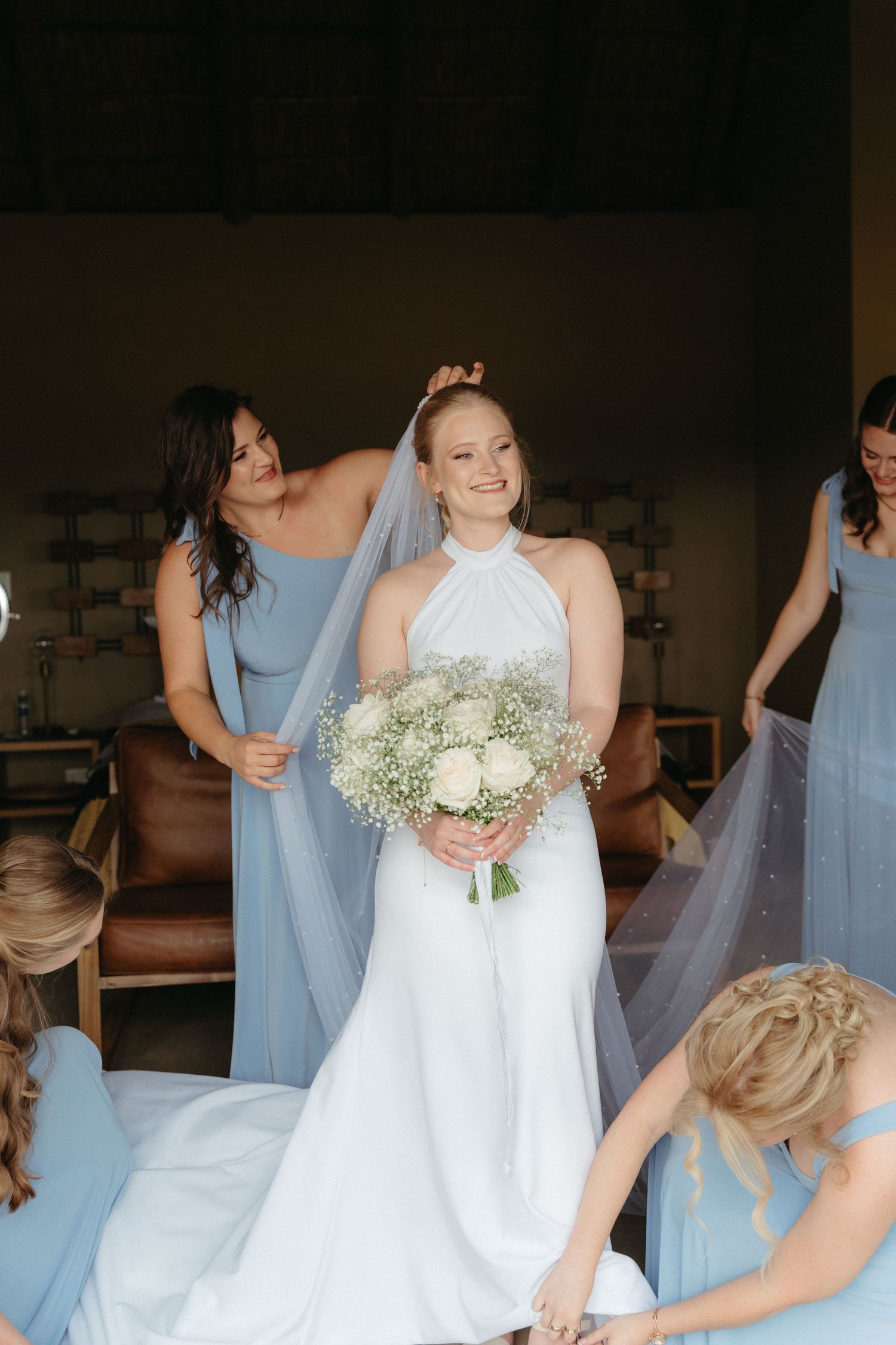Bridesmaids in pale blue dresses gather around bride holding white bouquet.