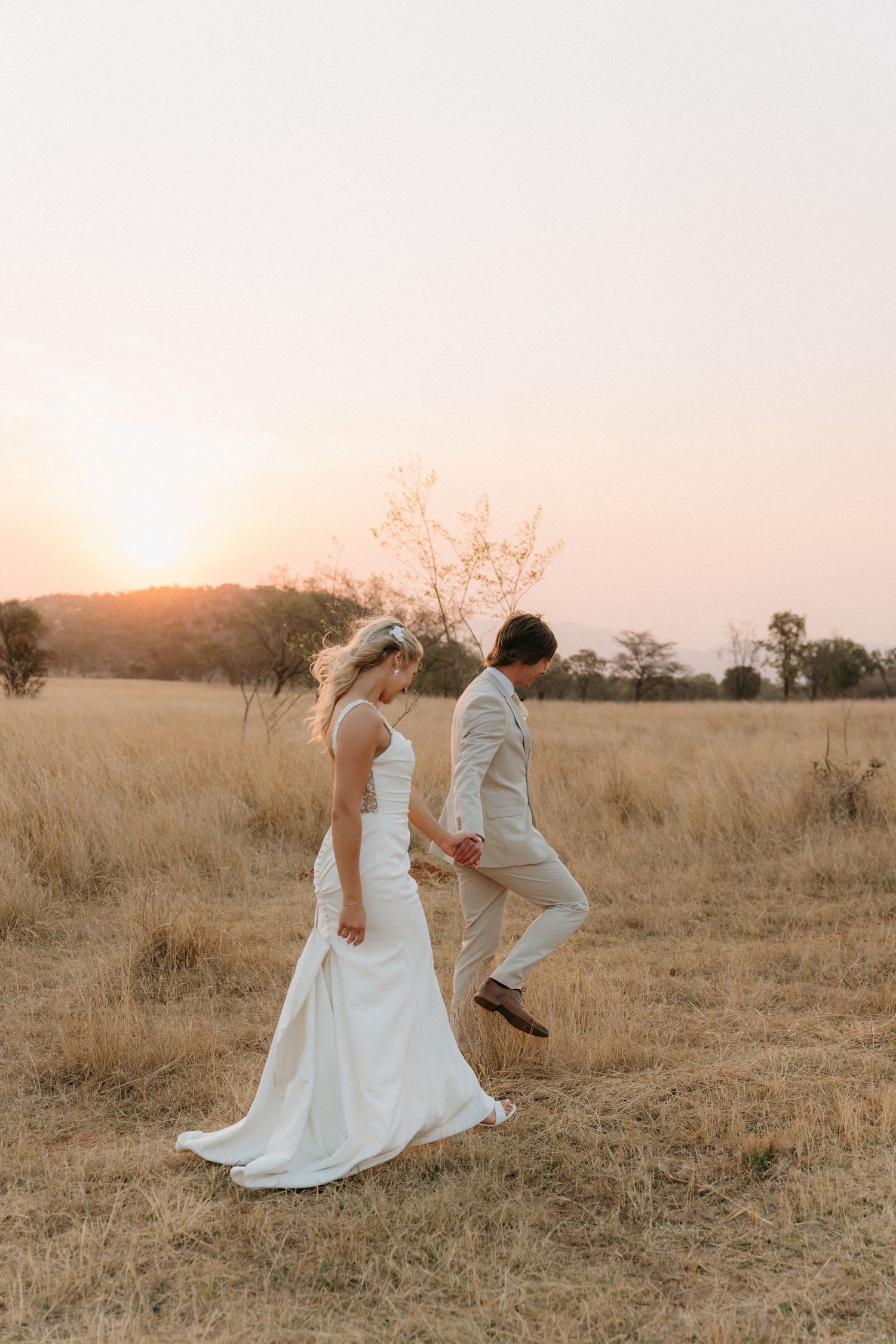 Newlyweds sharing a romantic dance in a sun-drenched field of tall grass.
