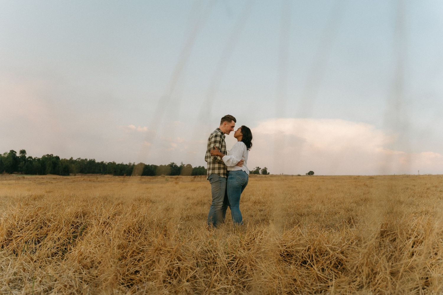 Wide landscape shot of a couple walking through a vast wheat field.