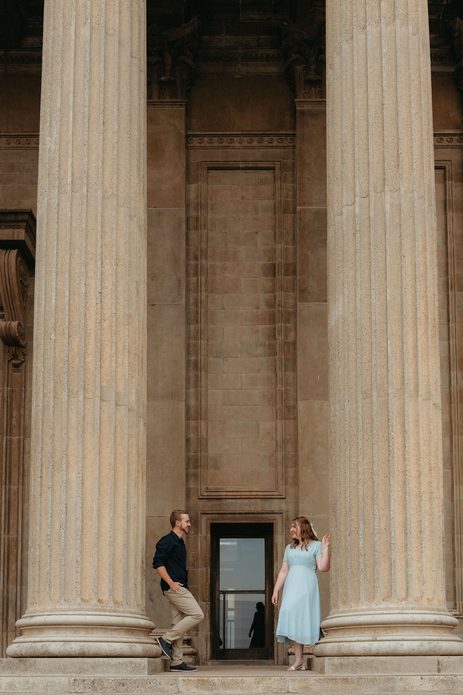 People sit between massive stone columns at the entrance of a grand neoclassical building, the Wits Great Hall