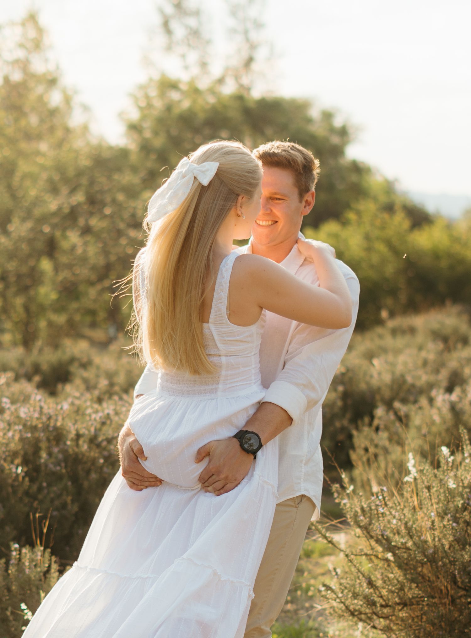 Couple embracing in golden sunlight among wild brush and flowers.
