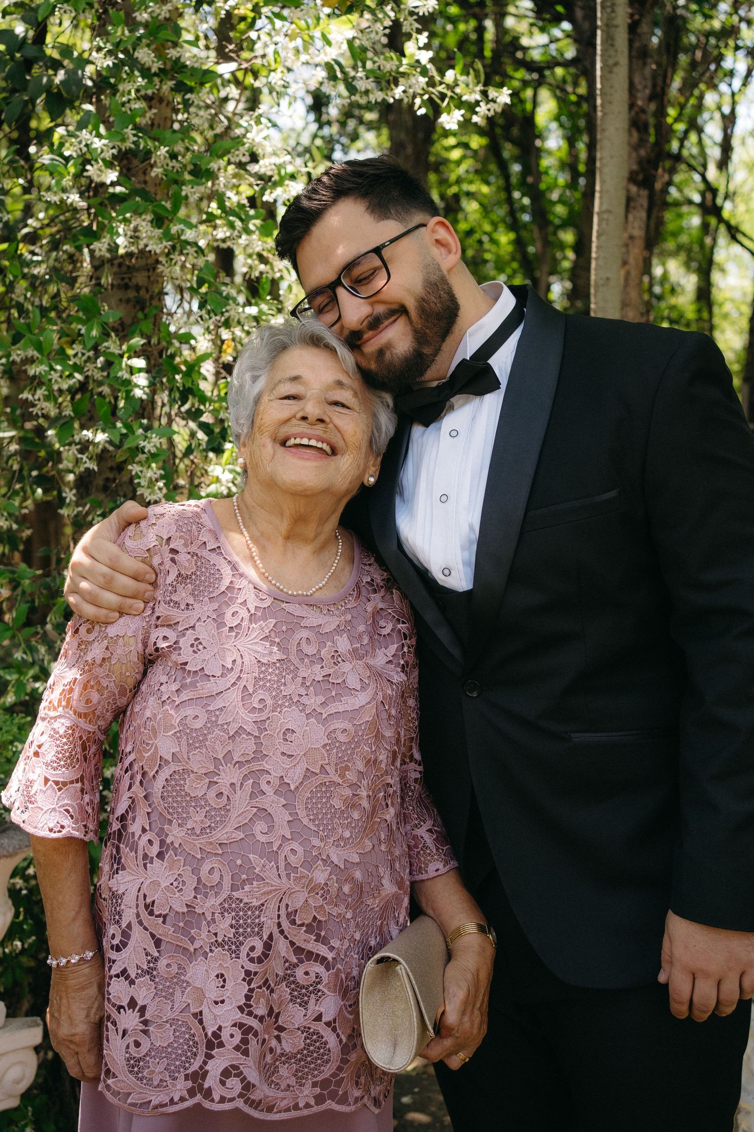A heartwarming moment captured outdoors showing two people embracing and smiling under flowering trees.