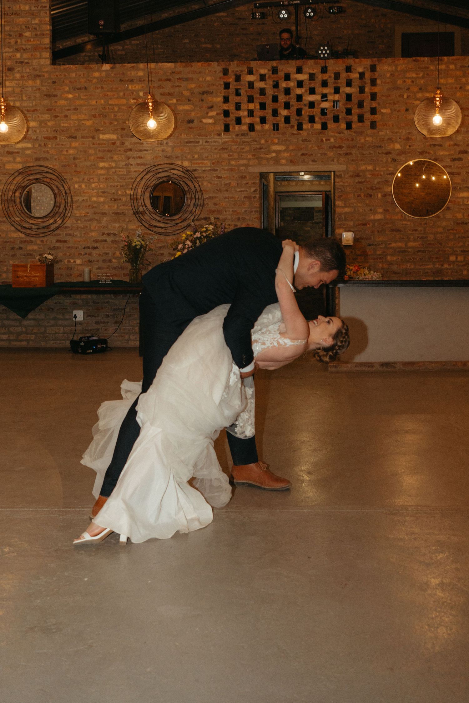 Dramatic dip during wedding dance in an industrial venue with exposed brick and pendant lights.