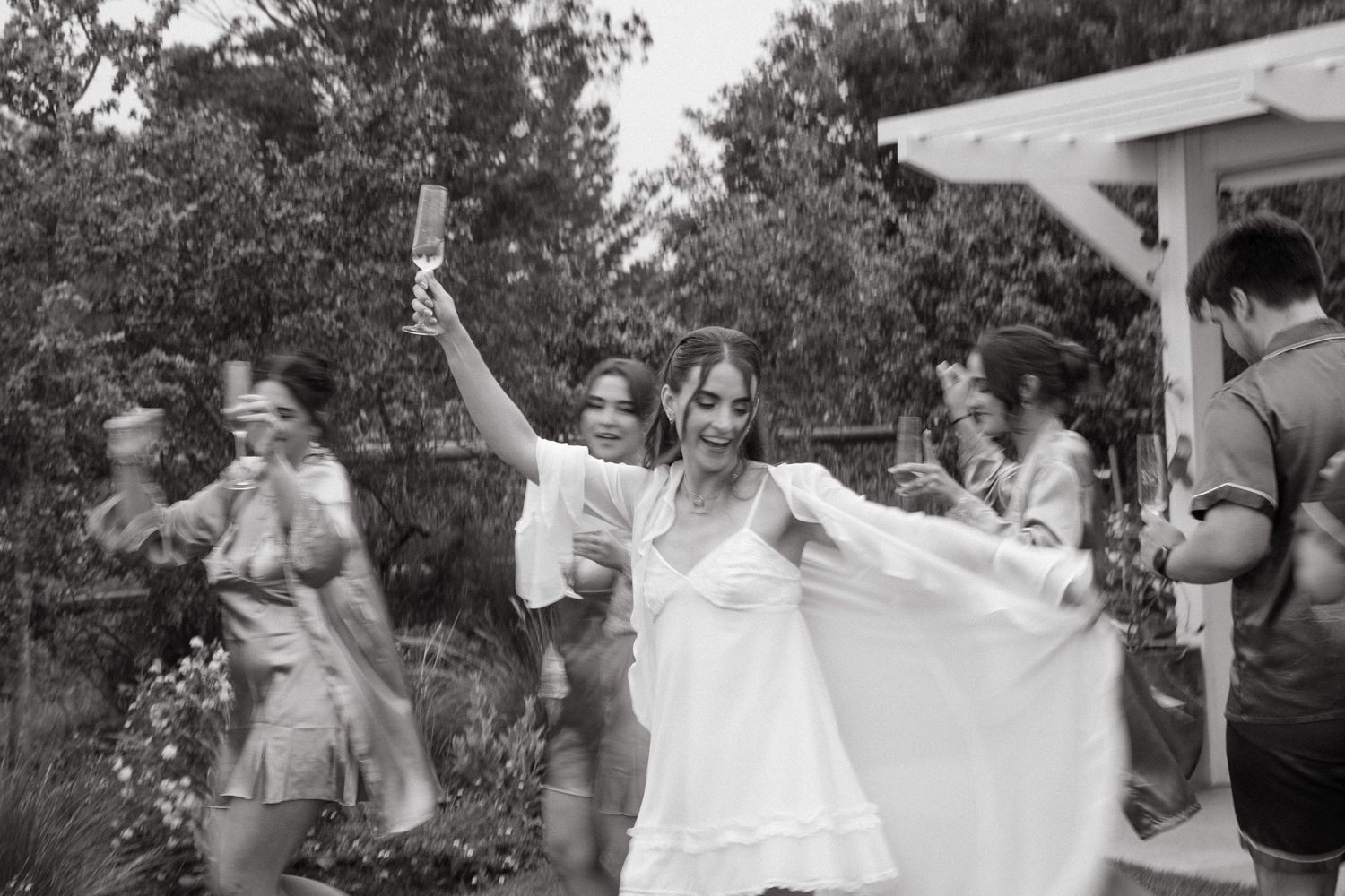 Bride in white dress dancing joyfully with bridal party outdoors in the Western Cape in black and white photo.