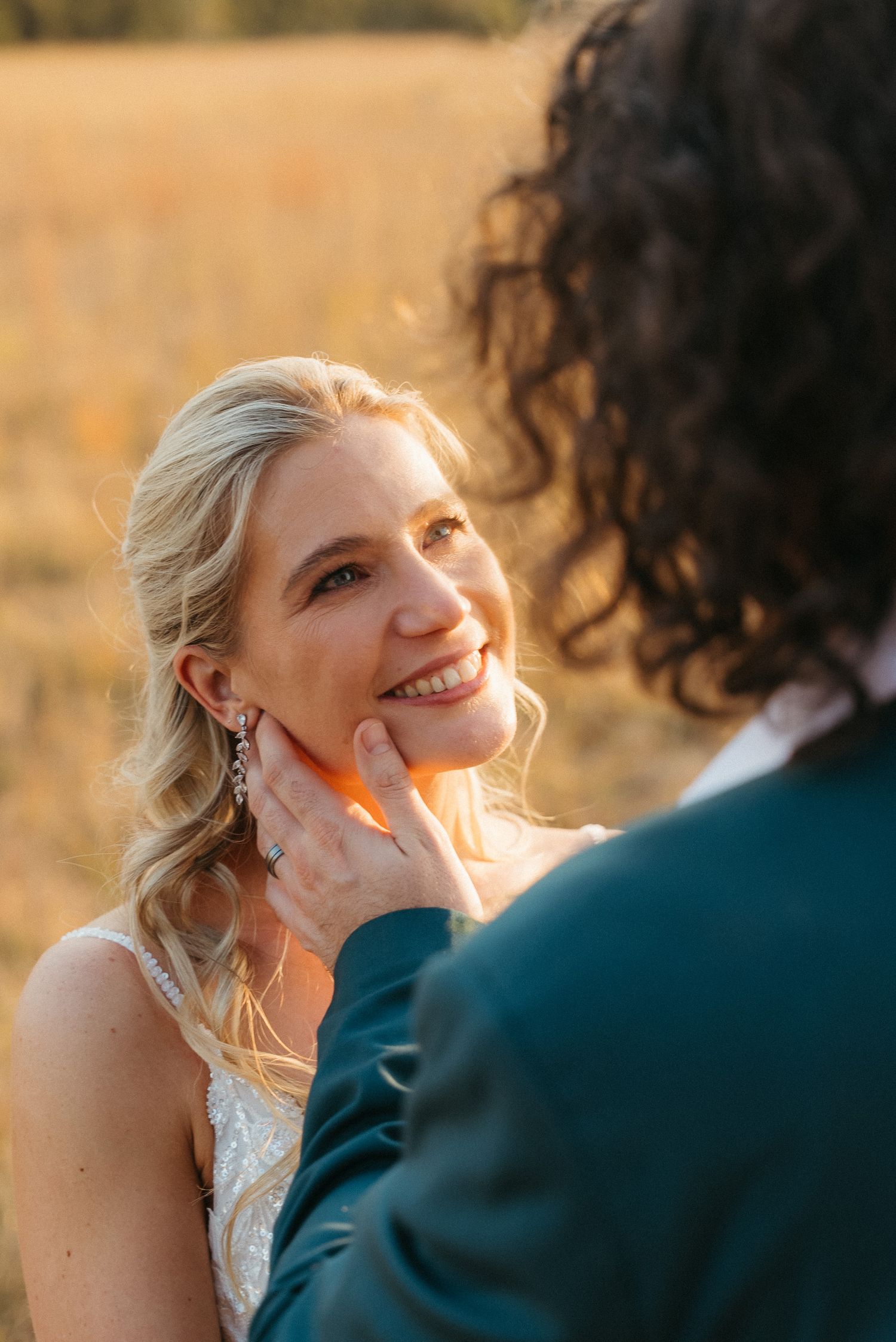 A bride smiles warmly as her groom gently cups her face during a golden hour outdoor wedding portrait.